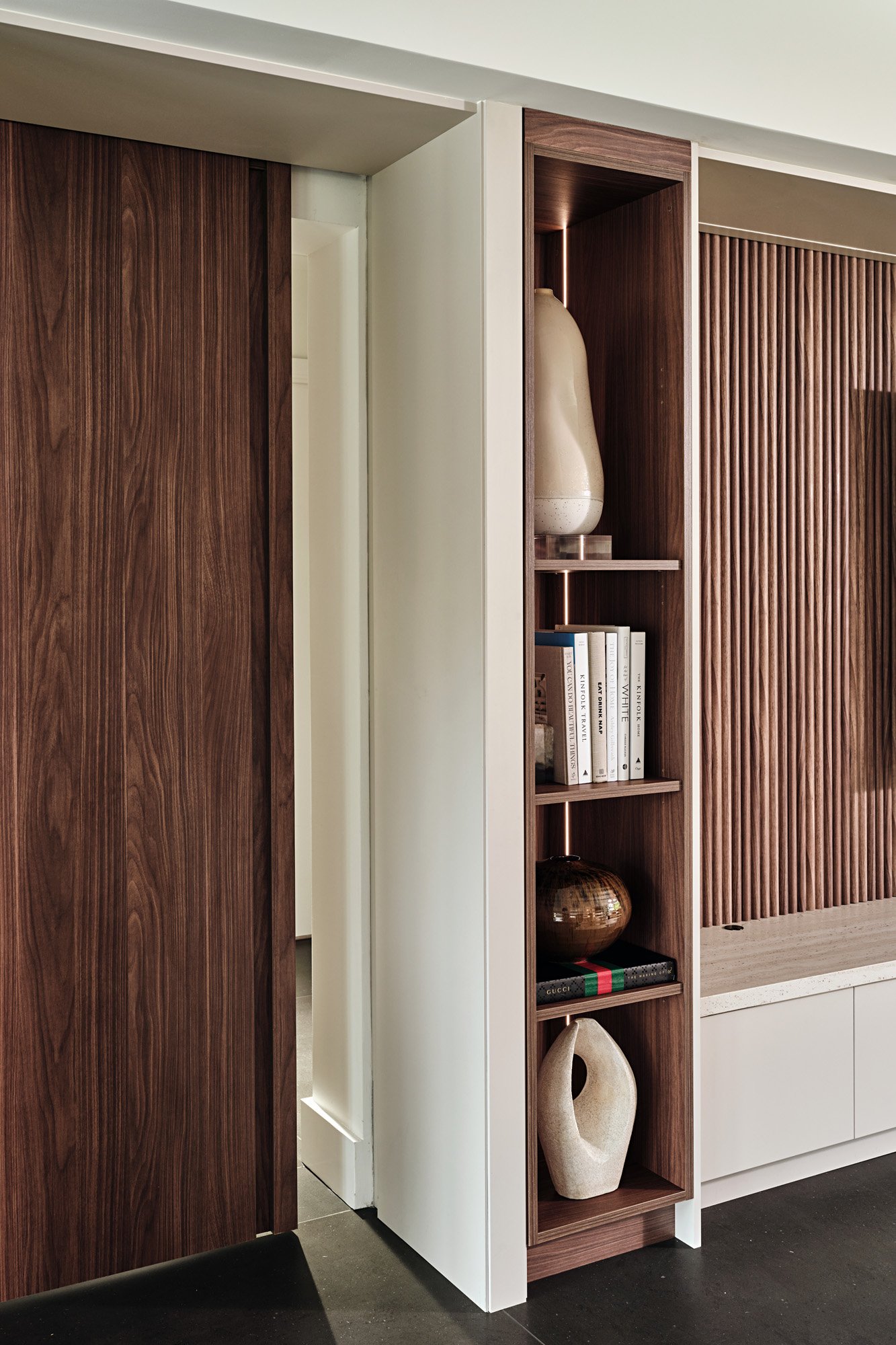 Walnut sliding pocket door beside lit display shelving
