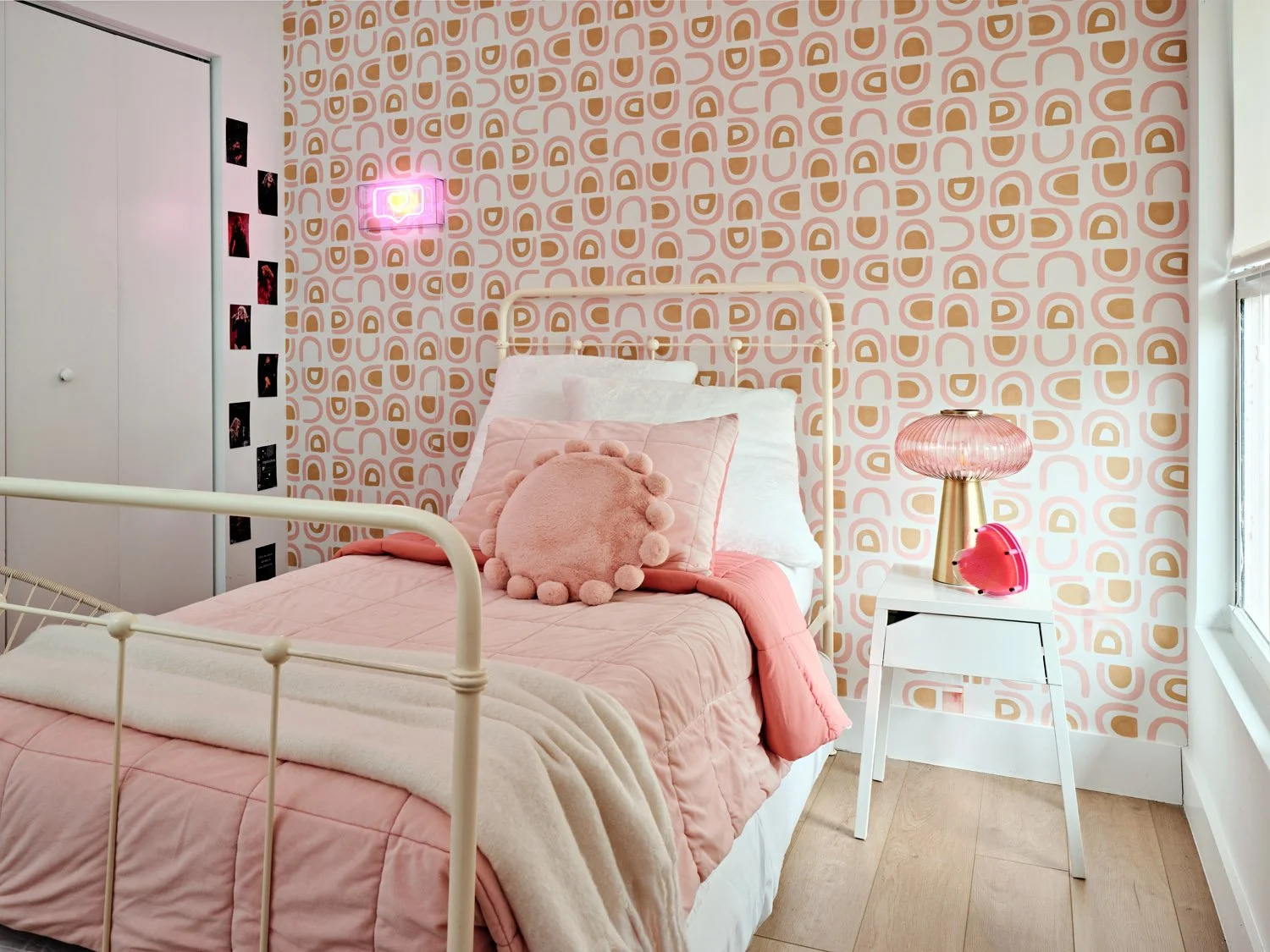 Pink bedroom with white iron bed, patterned wallpaper and bedside table