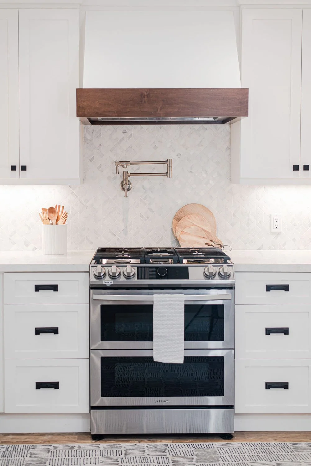 Stainless double oven range under a white hood with walnut trim