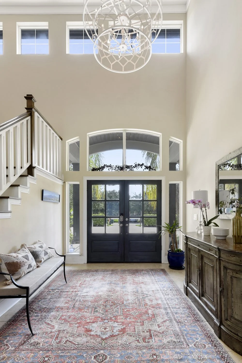 Tall foyer with sphere chandelier, staircase and patterned rug