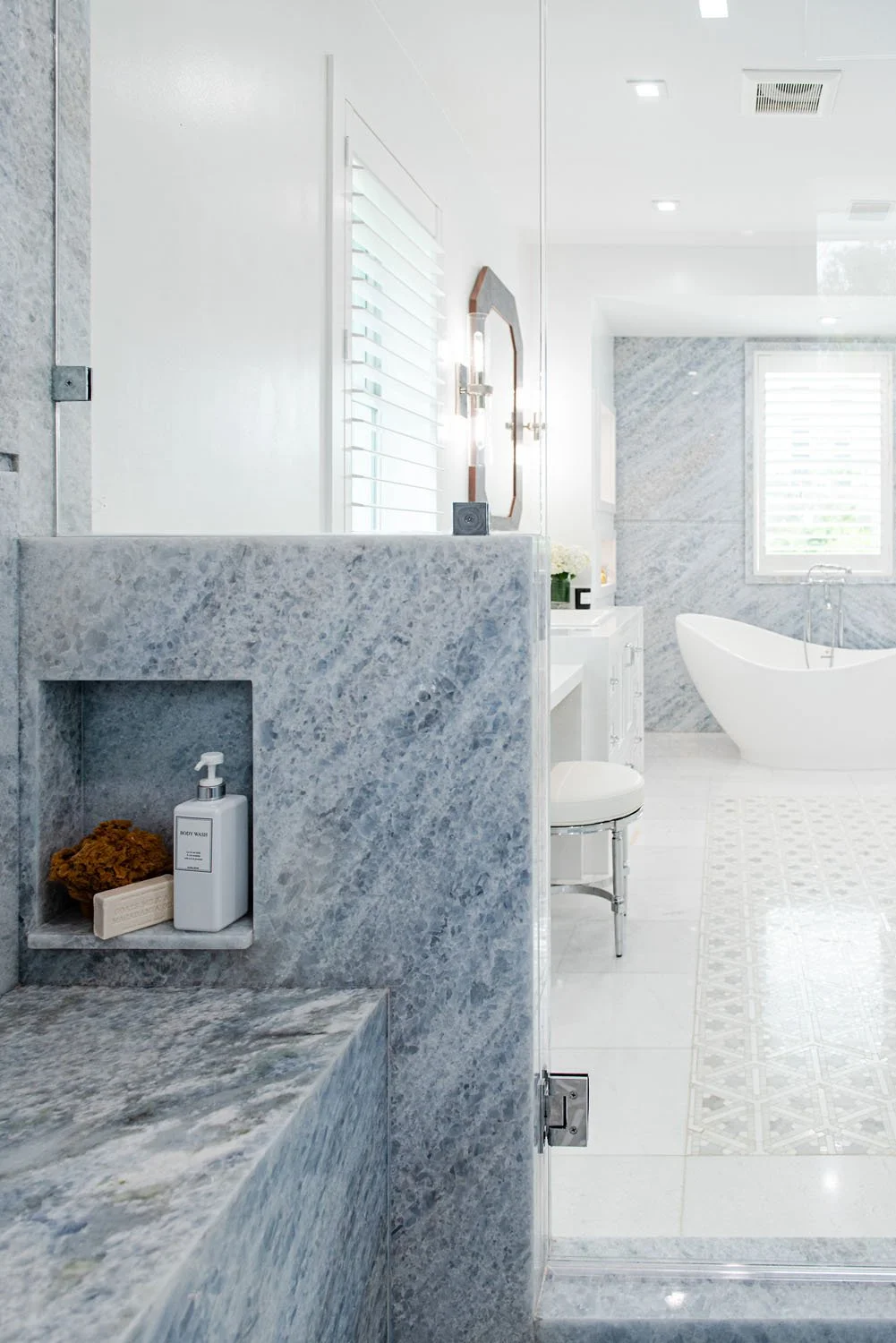 Marble shower niche with glass door and view of vanity