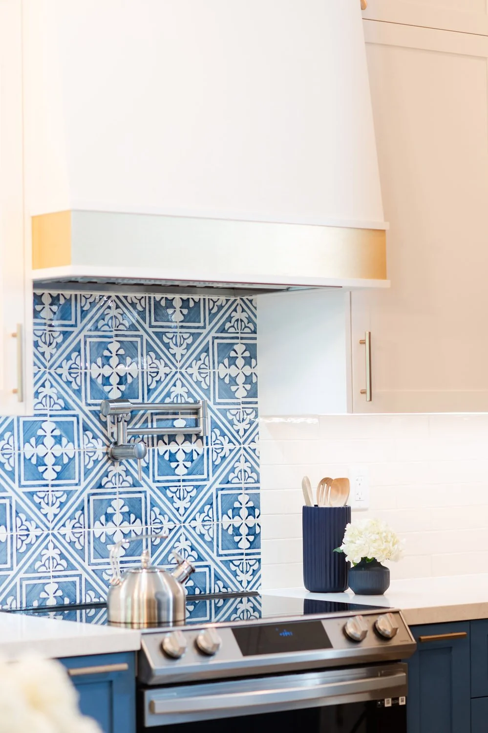 Range with white hood, brass trim and blue patterned tile backsplash