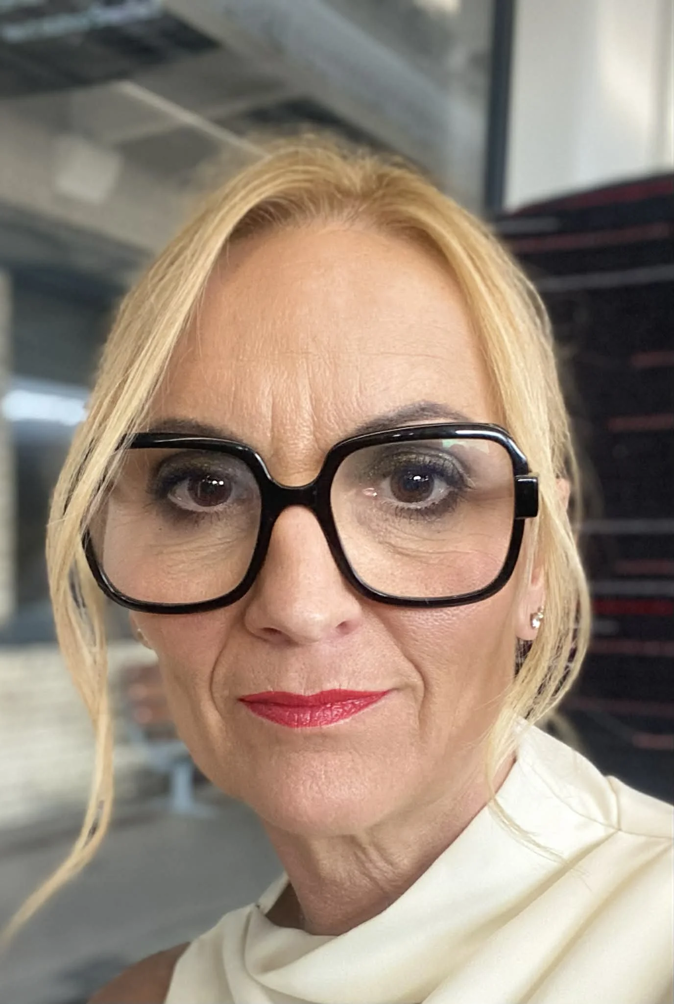 A woman with blonde hair and black glasses smiling against a white background.