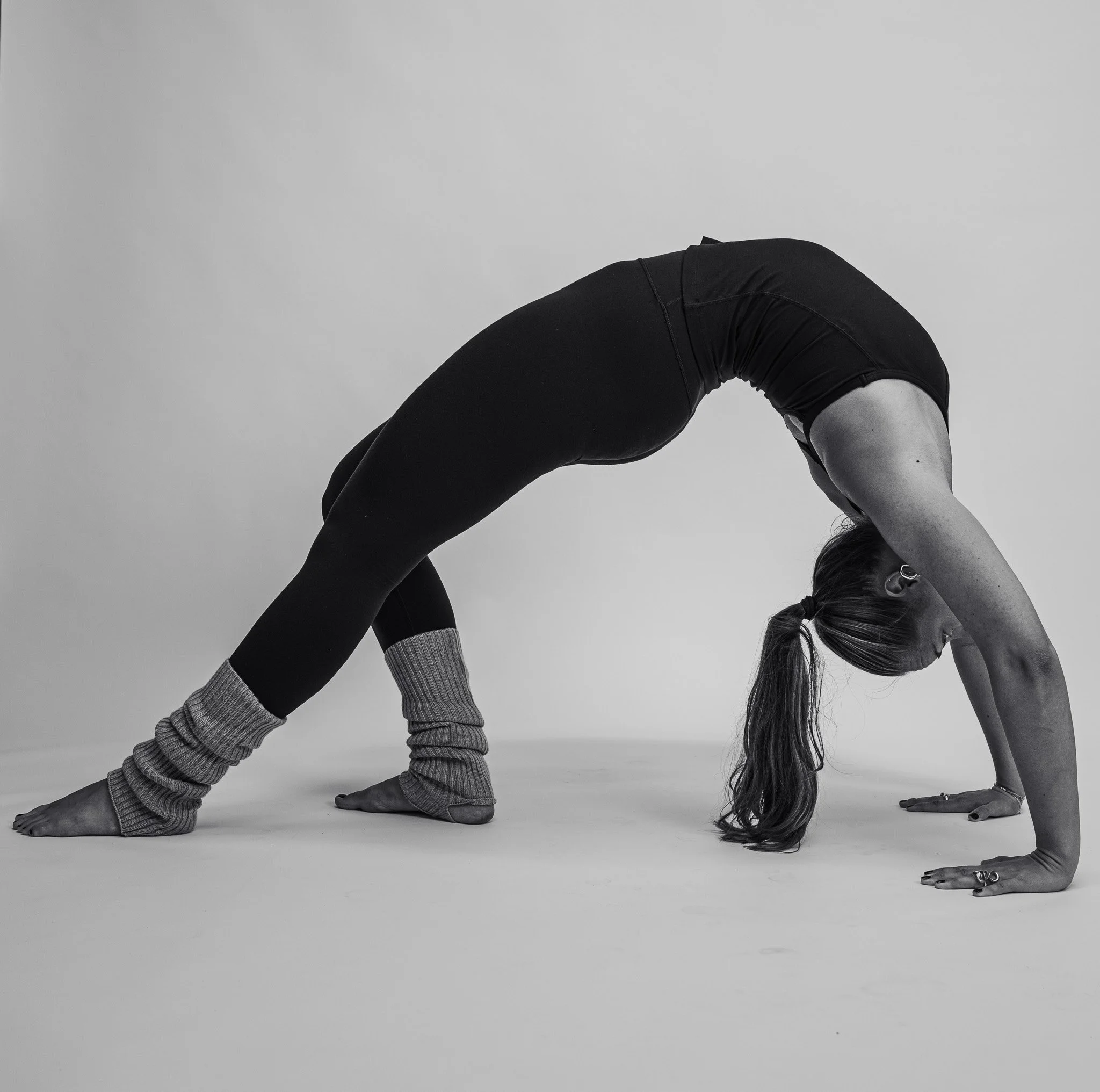 Sort-hvid foto af en person i en yoga-position med bøjet ryg, hænder og fødder på gulvet, omgivet af filthat.