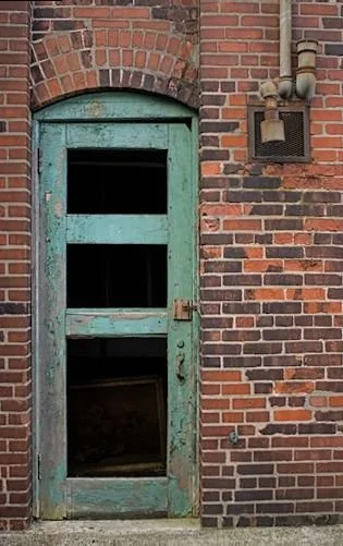 Old weathered green door with three open panels set in a brick wall with an arched brick top.