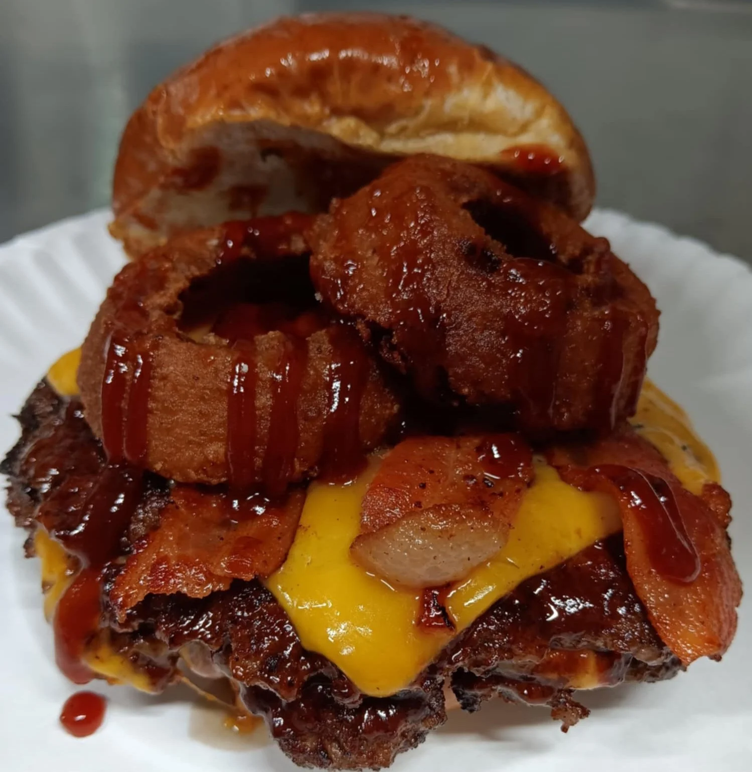 A close-up of a burger with bacon, cheese, and barbecue sauce on a white plate.