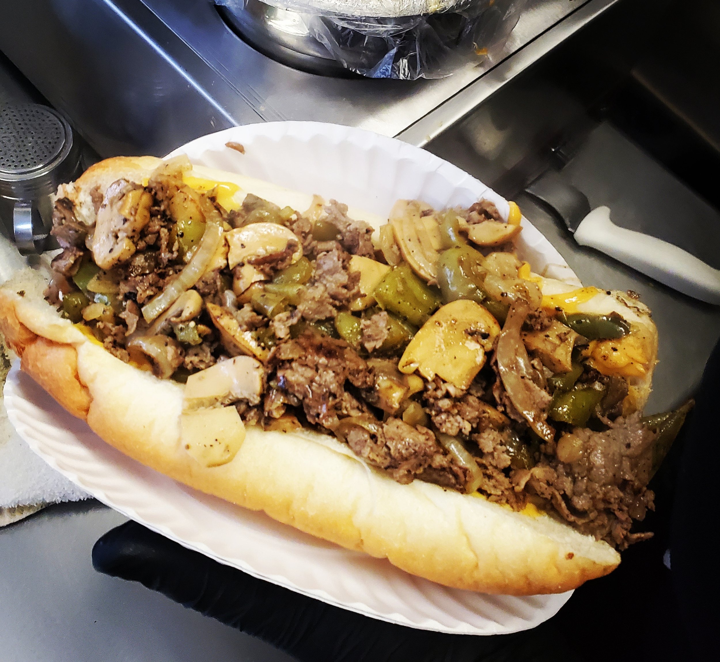A hot dog in a white bun topped with cooked ground beef and sautéed green bell peppers.