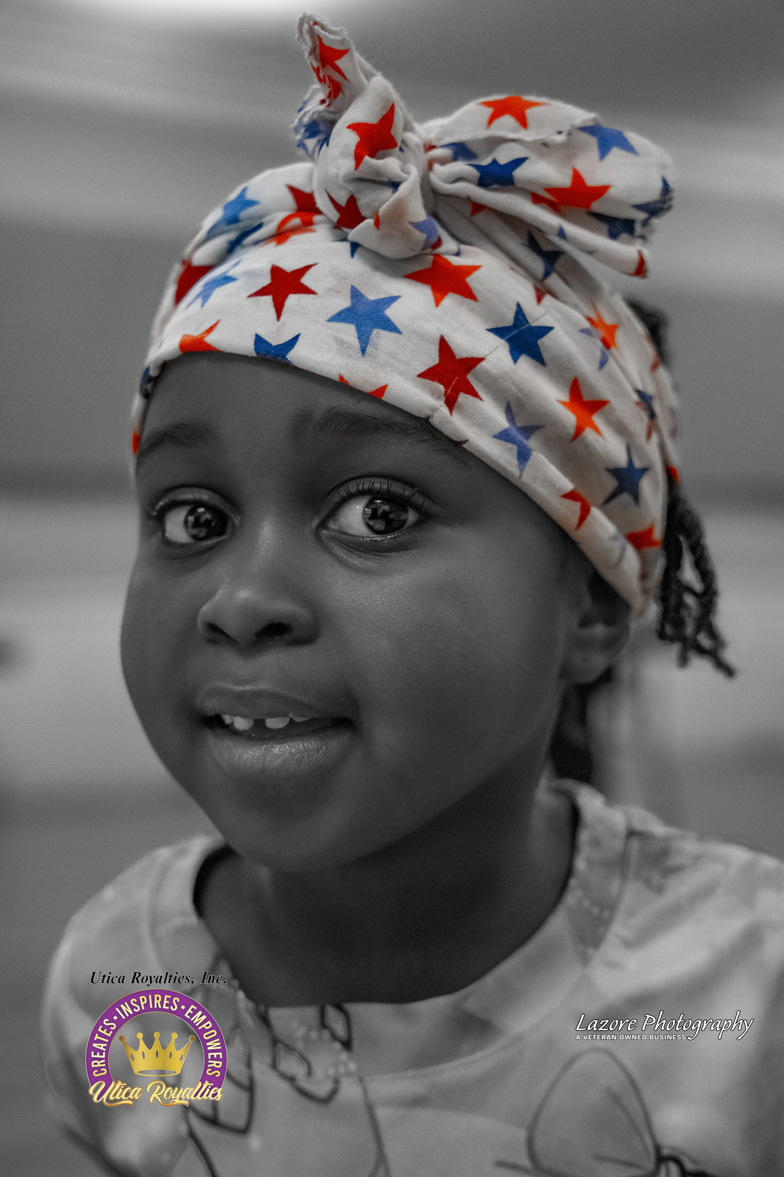 Close-up of a young girl wearing a star-patterned headscarf, smiling, in black and white with selective color on the headscarf. Logo and photography credits in the bottom corners.
