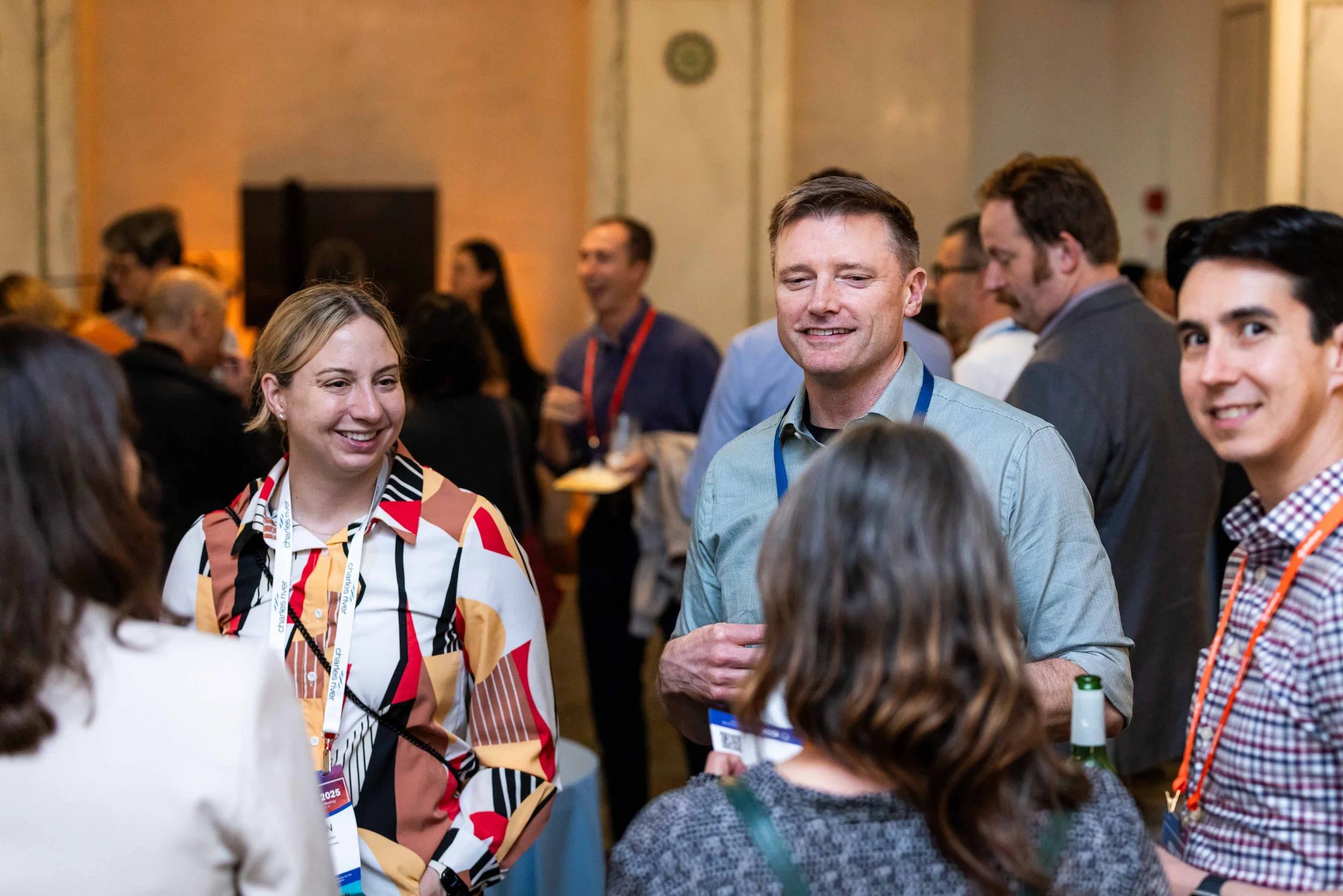 People socializing at a conference, engaging in conversation, wearing name badges, in a well-lit room.