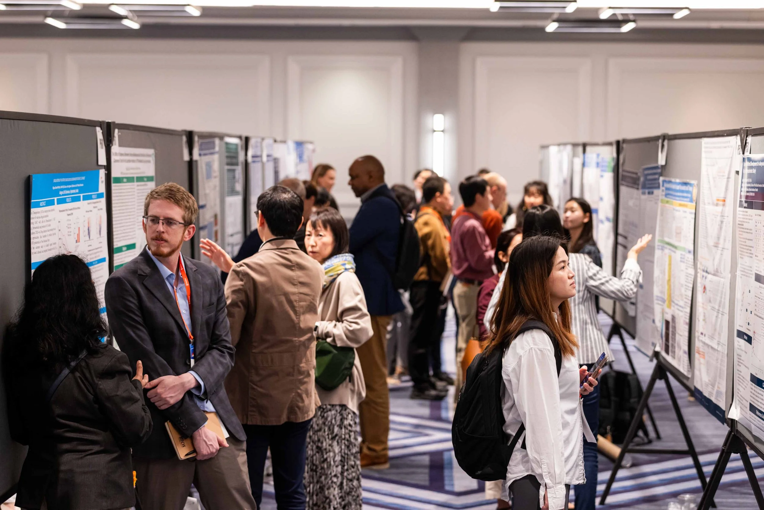 People attending a scientific research conference and viewing research posters on display boards in a conference room.