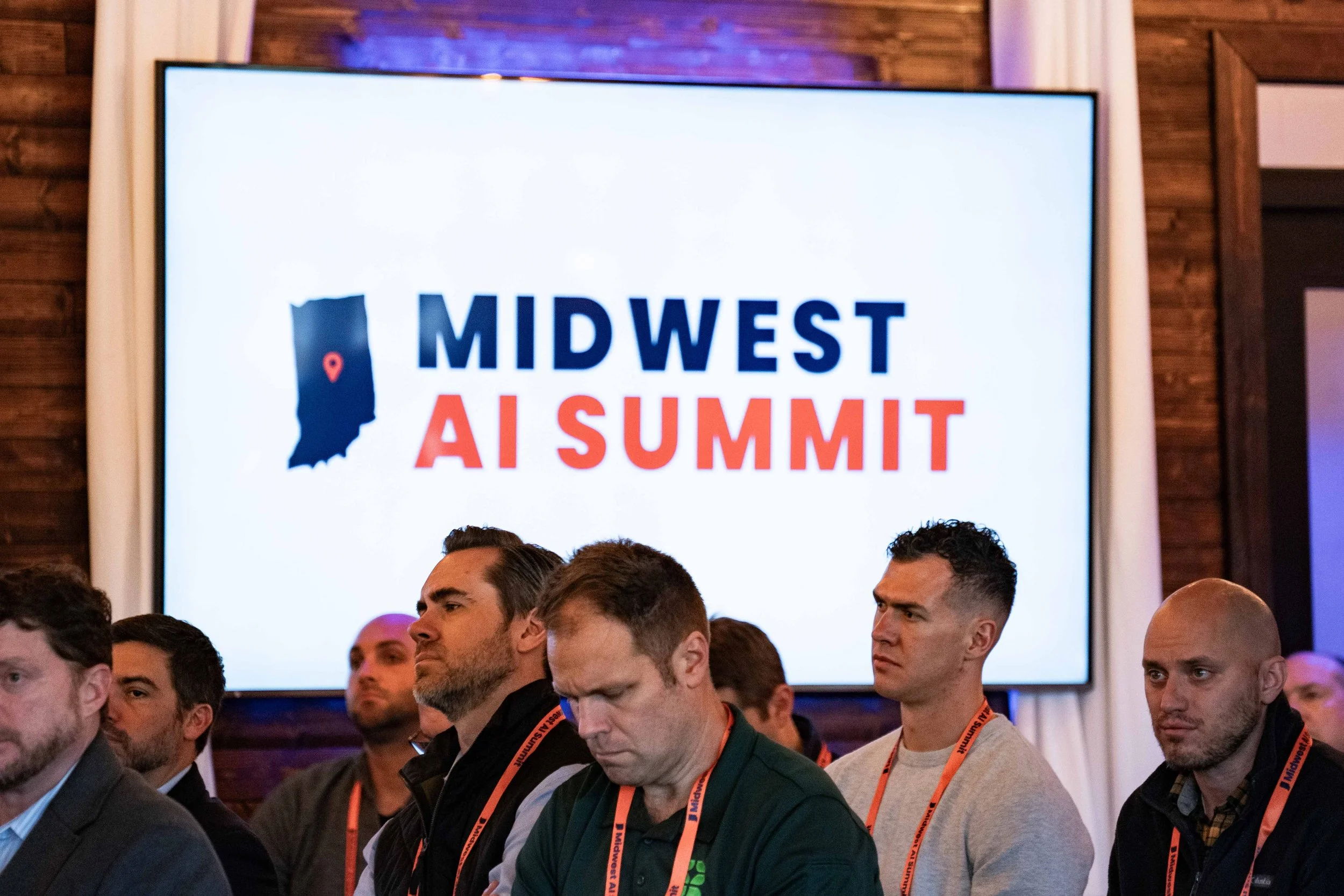 Attendees at the Midwest AI Summit seated and listening, with a large screen behind them displaying the event logo.