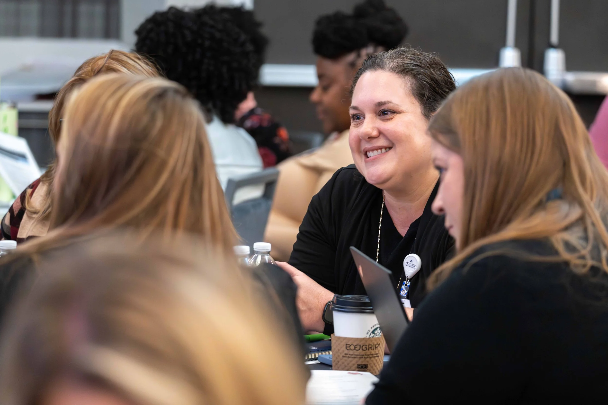 A group of women engaged in conversation at a conference or workshop, with one woman smiling in focus.
