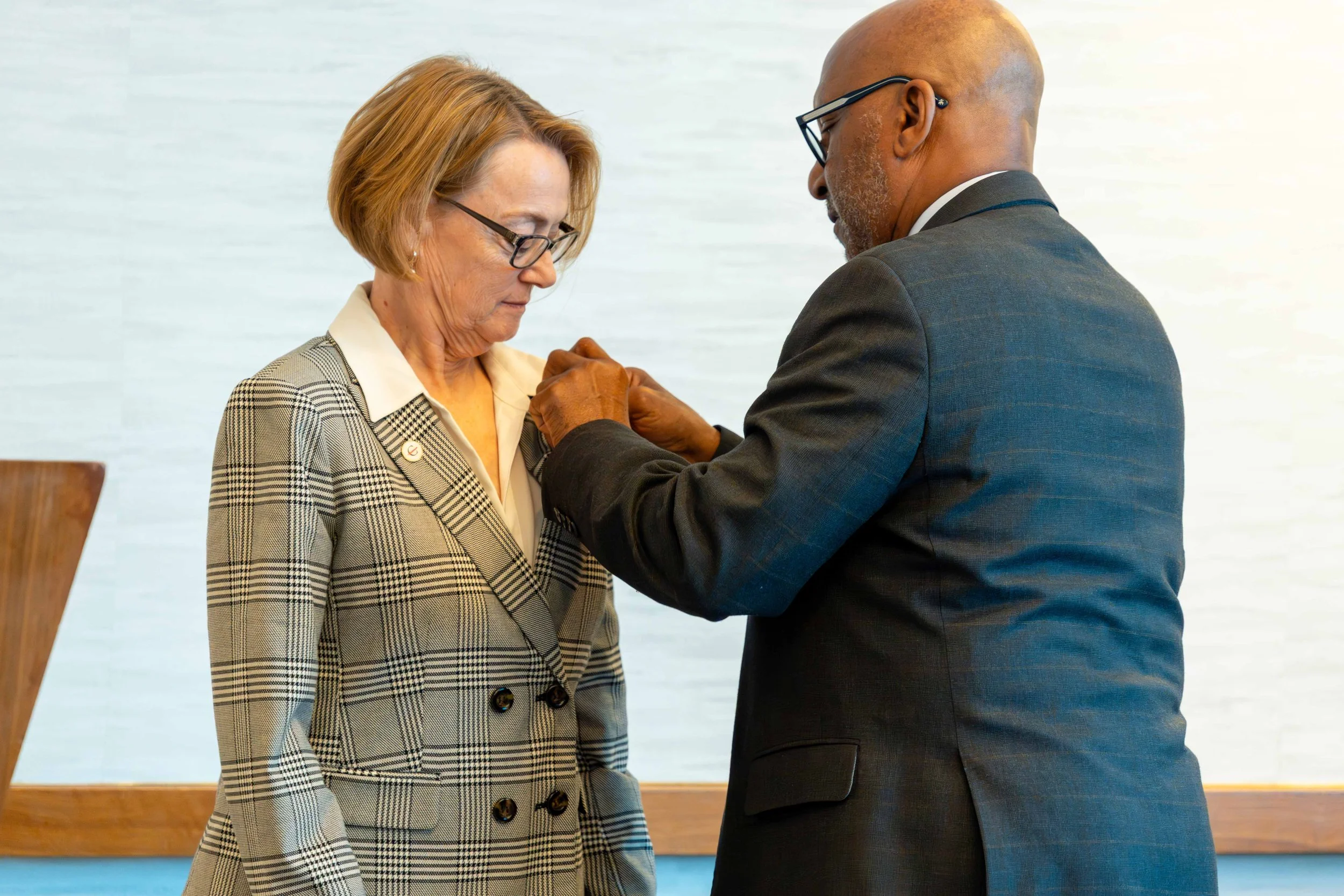 A man is pinning a badge on a woman's blazer during an award ceremony or recognition event.