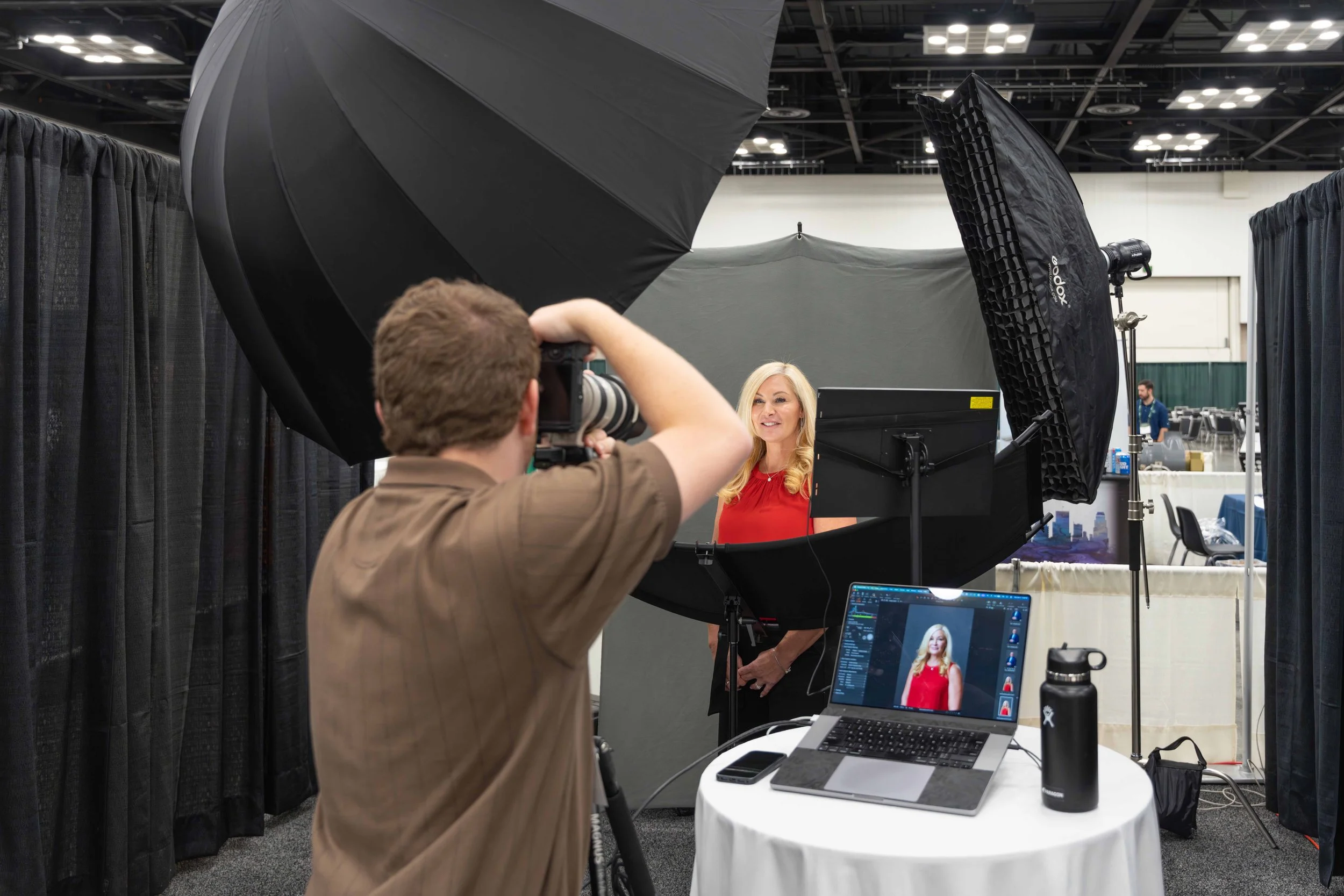 Photographer taking pictures of a woman in a red dress during a professional photoshoot at an indoor event.