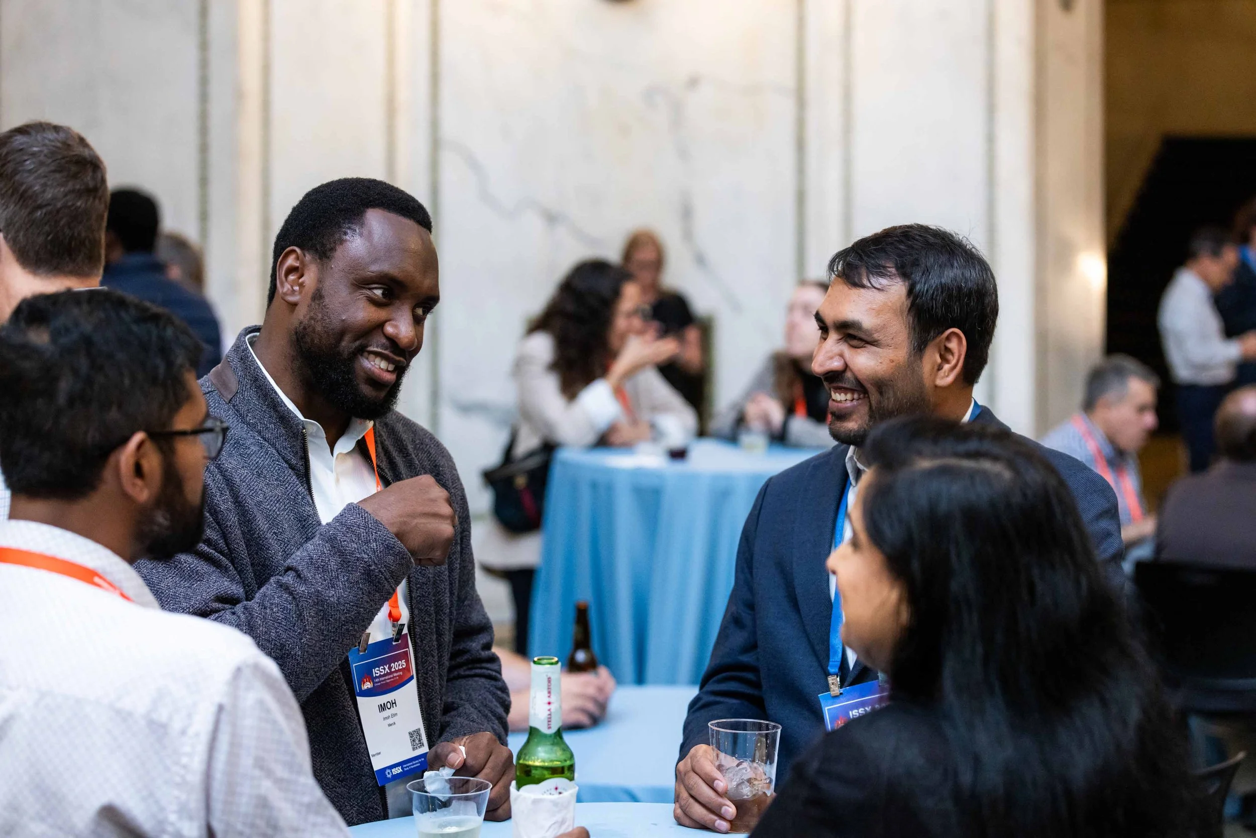 Group of diverse professionals talking and smiling at a conference or networking event, with name tags visible.