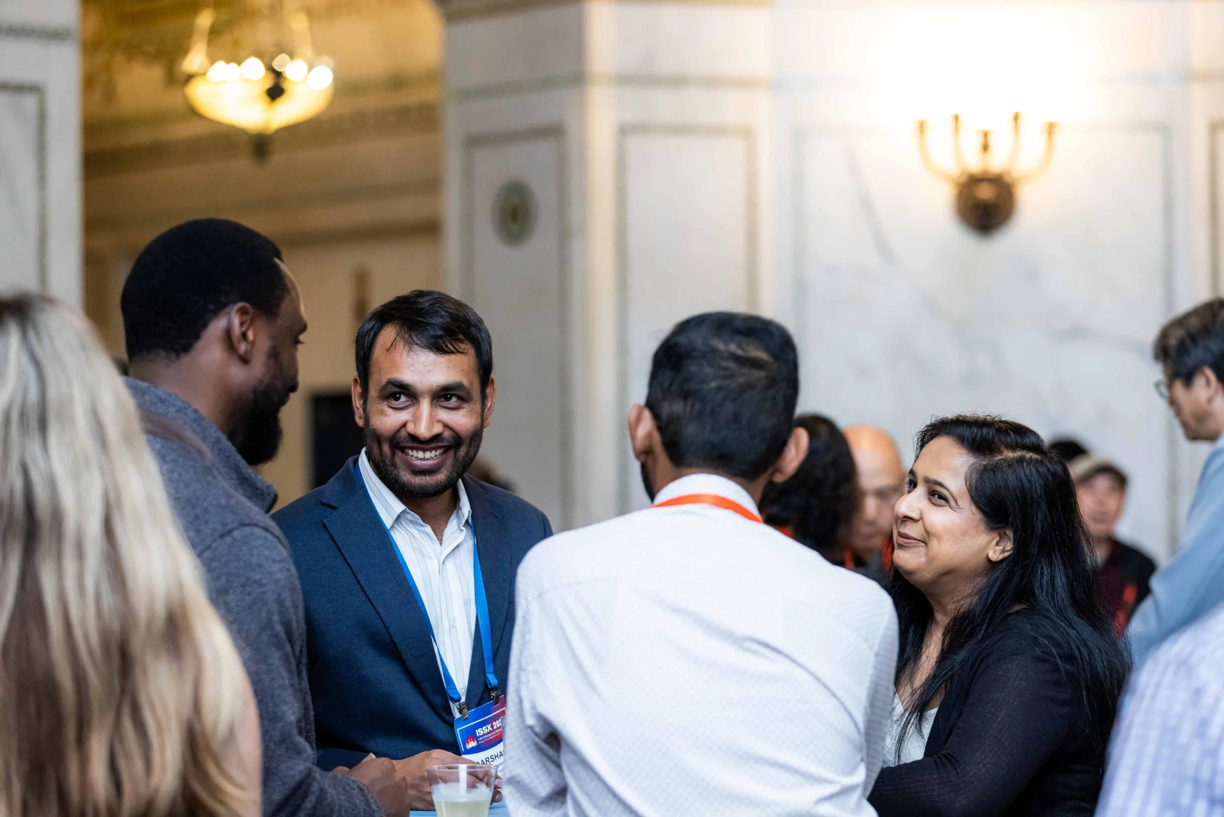 A group of diverse professionals engaged in conversation at a conference or networking event, with people smiling and exchanging ideas.