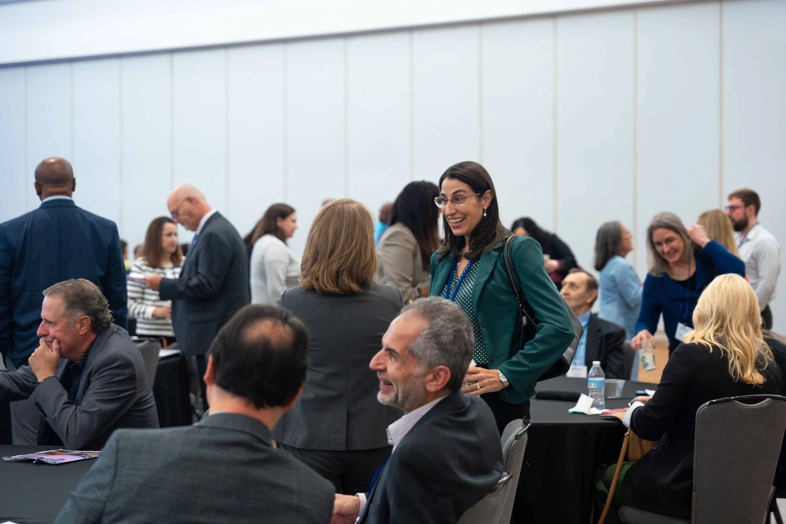 People at a professional conference or seminar engaged in conversations and networking, with some sitting at tables and others standing.