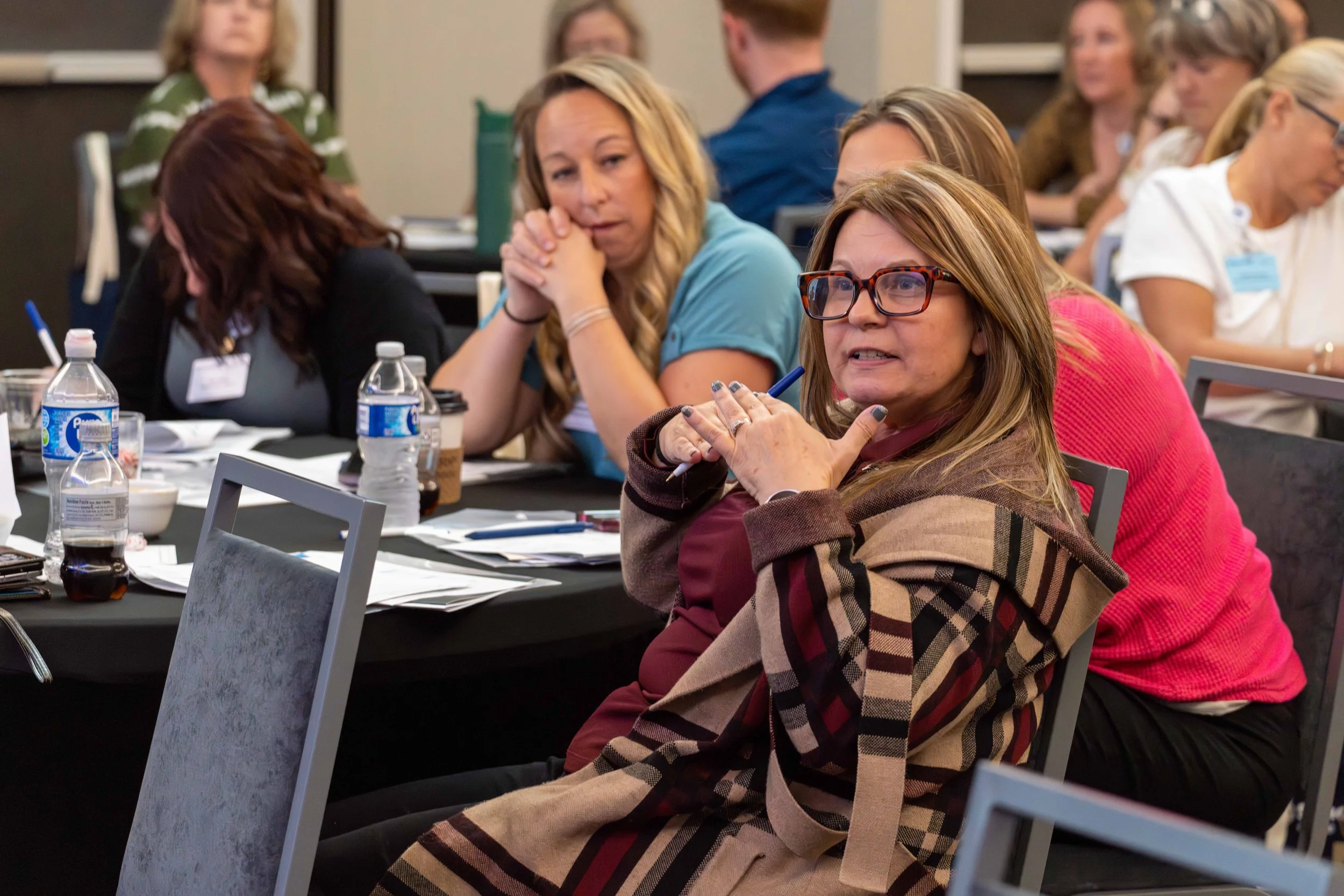 Group of women sitting at tables during a conference or workshop, engaging in discussion and listening attentively.