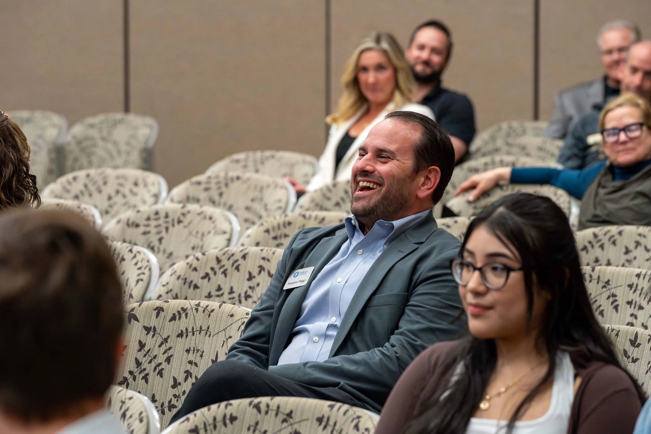 Group of people seated in a conference room, smiling and laughing.