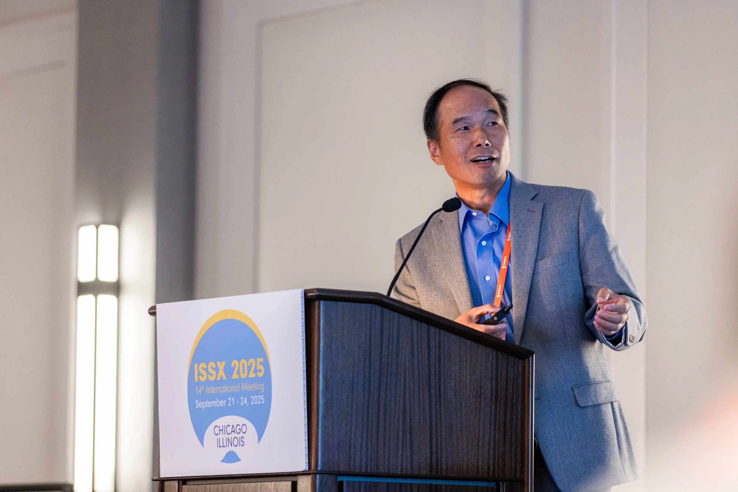 A man in a grey suit giving a presentation at a conference with a sign that reads ISSX 2025, 14th International Meeting, September 21-24, 2025, Chicago, Illinois.