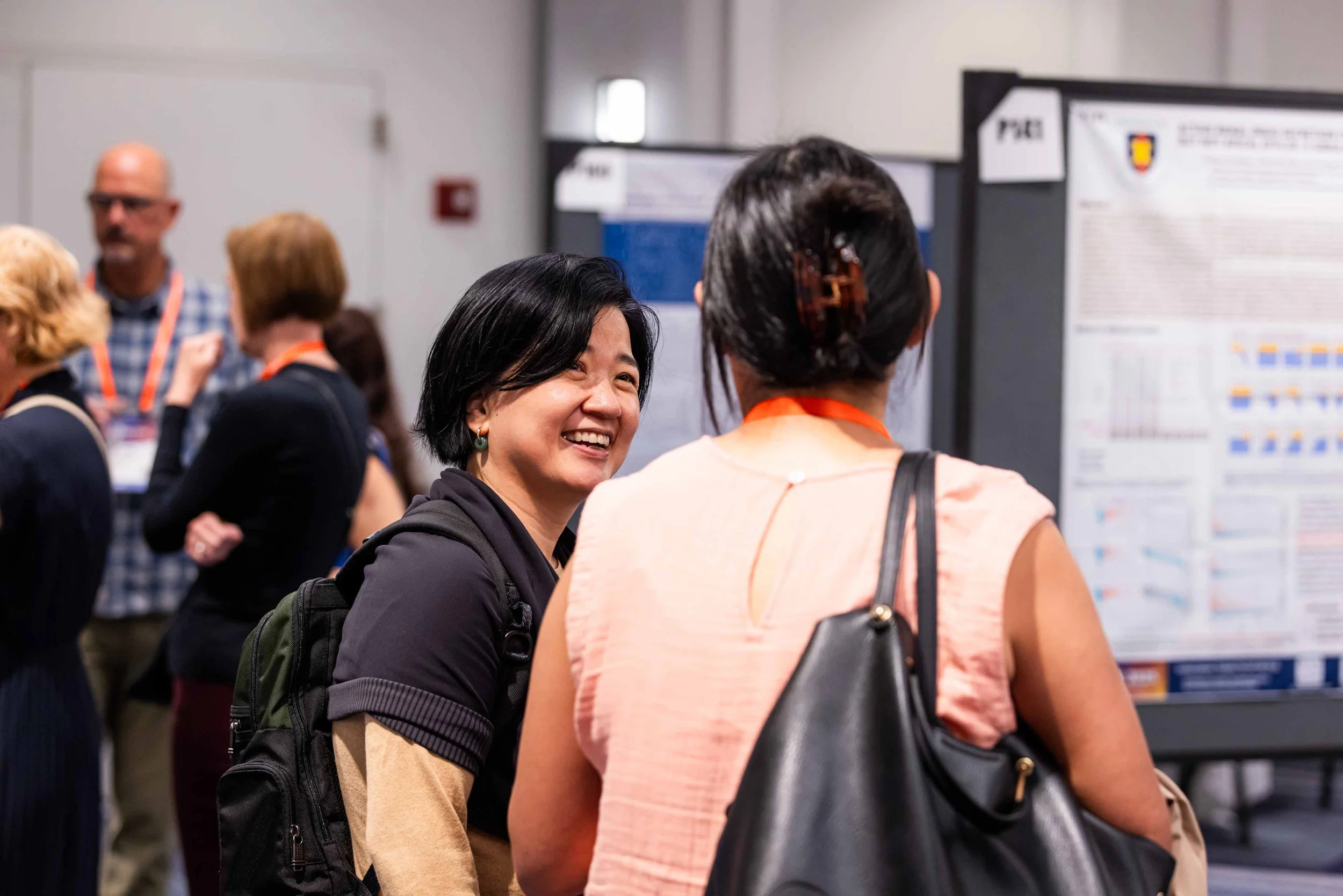 Two women talking at an academic conference, with poster presentations in the background.