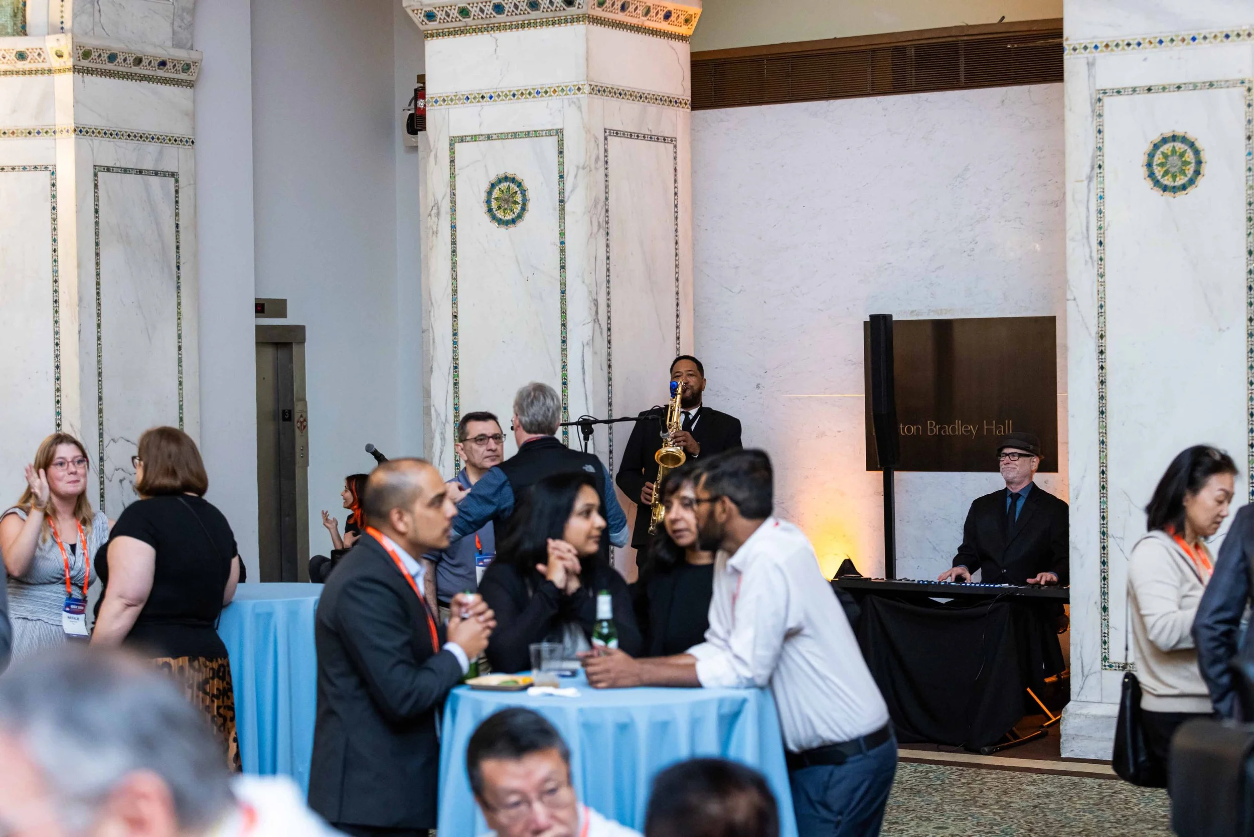 People at a social event in a hall with jazz musicians playing live music in the background.