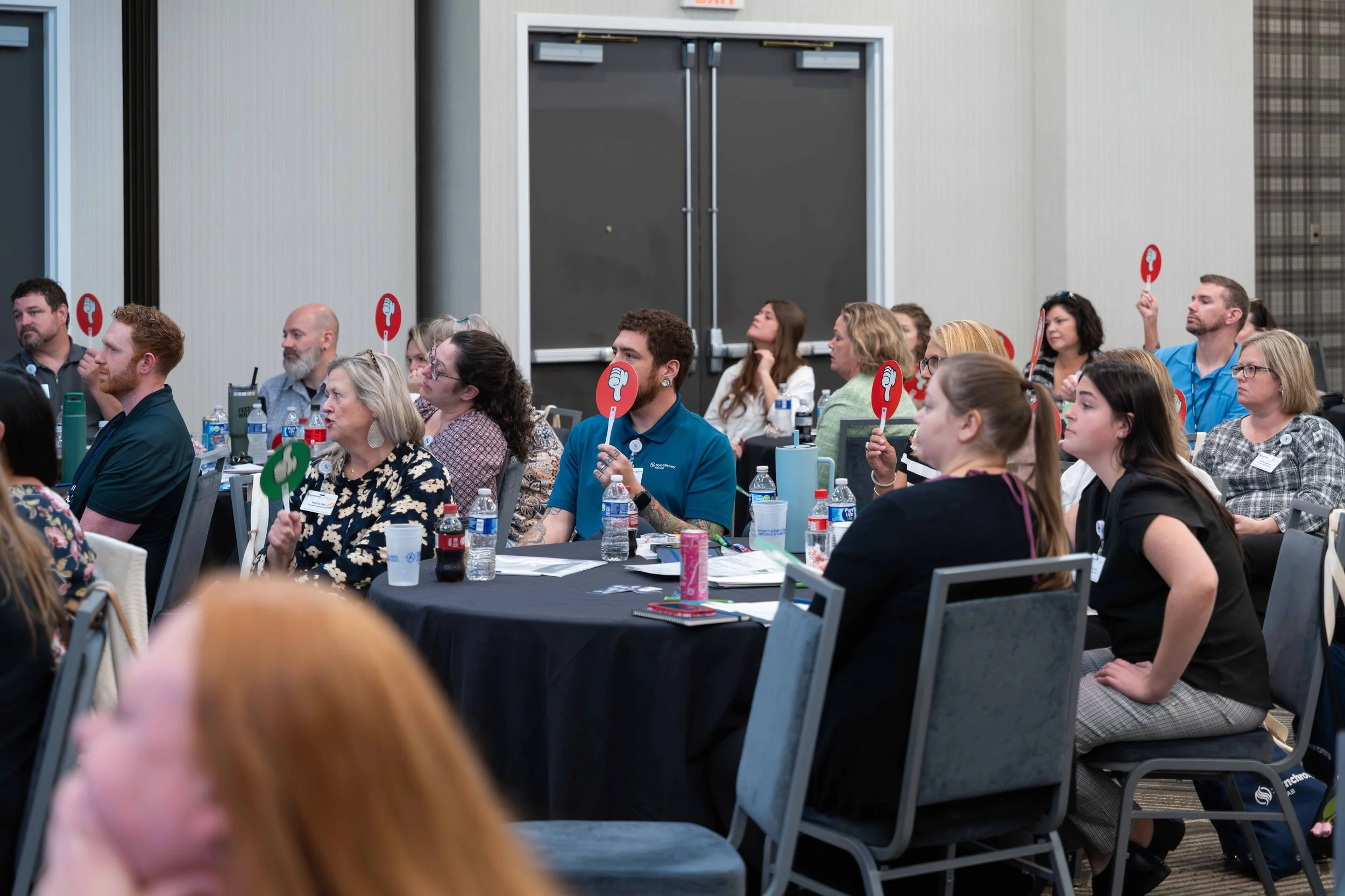 Audience at a conference or seminar, with some attendees holding up signs with thumbs-up or thumbs-down symbols.