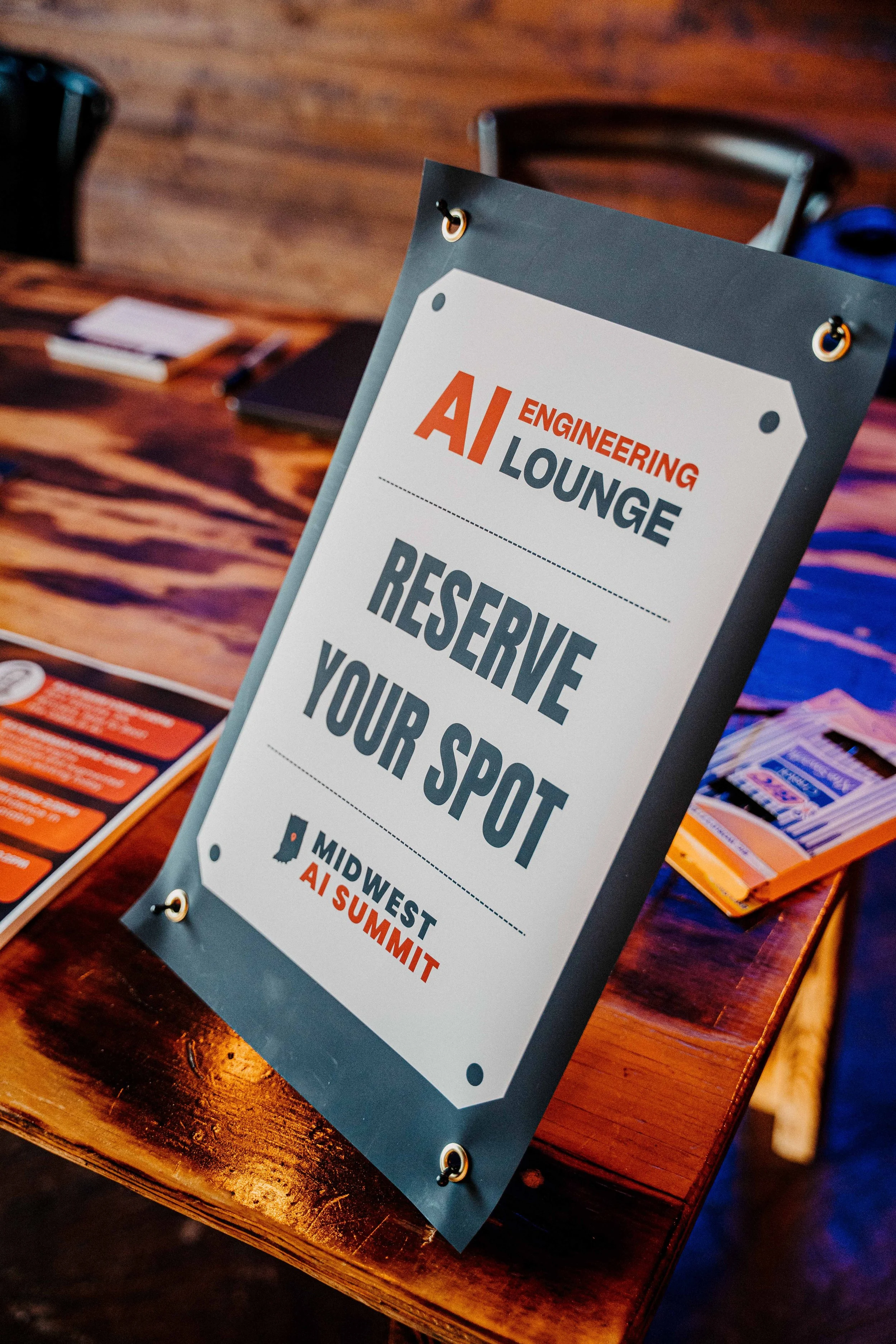 Sign on a table at a conference room reads 'AI Engineering Lounge Reserve Your Spot' with 'Midwest AI Summit' logo at the bottom.