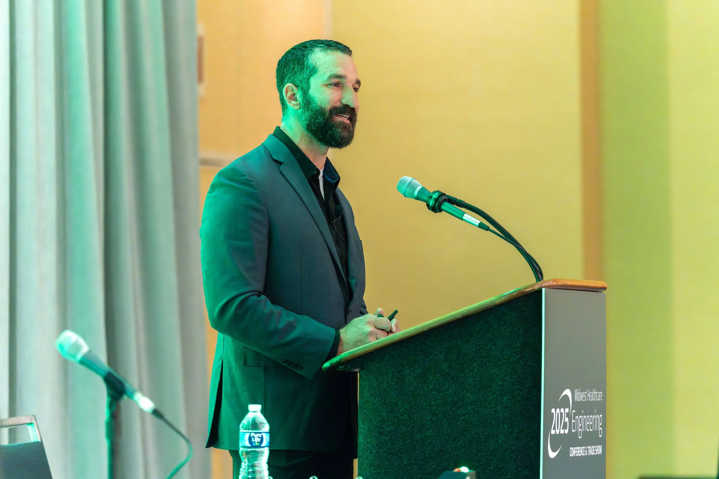 A man in a suit standing at a podium with a microphone, speaking at a conference.