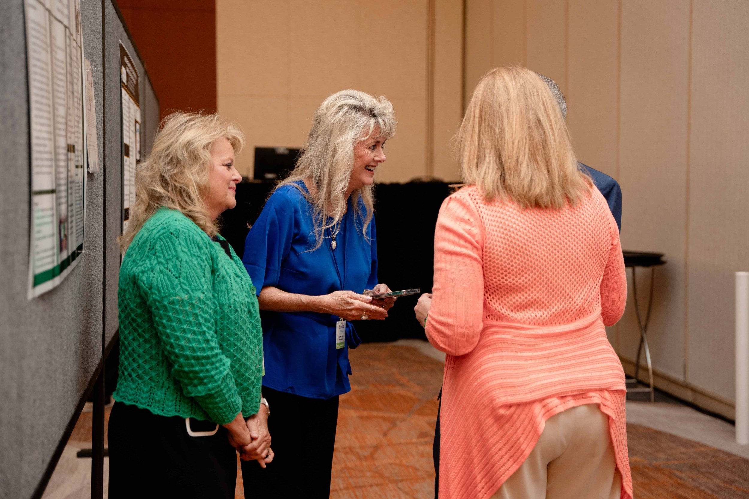 Four women standing and talking in a conference or event room.