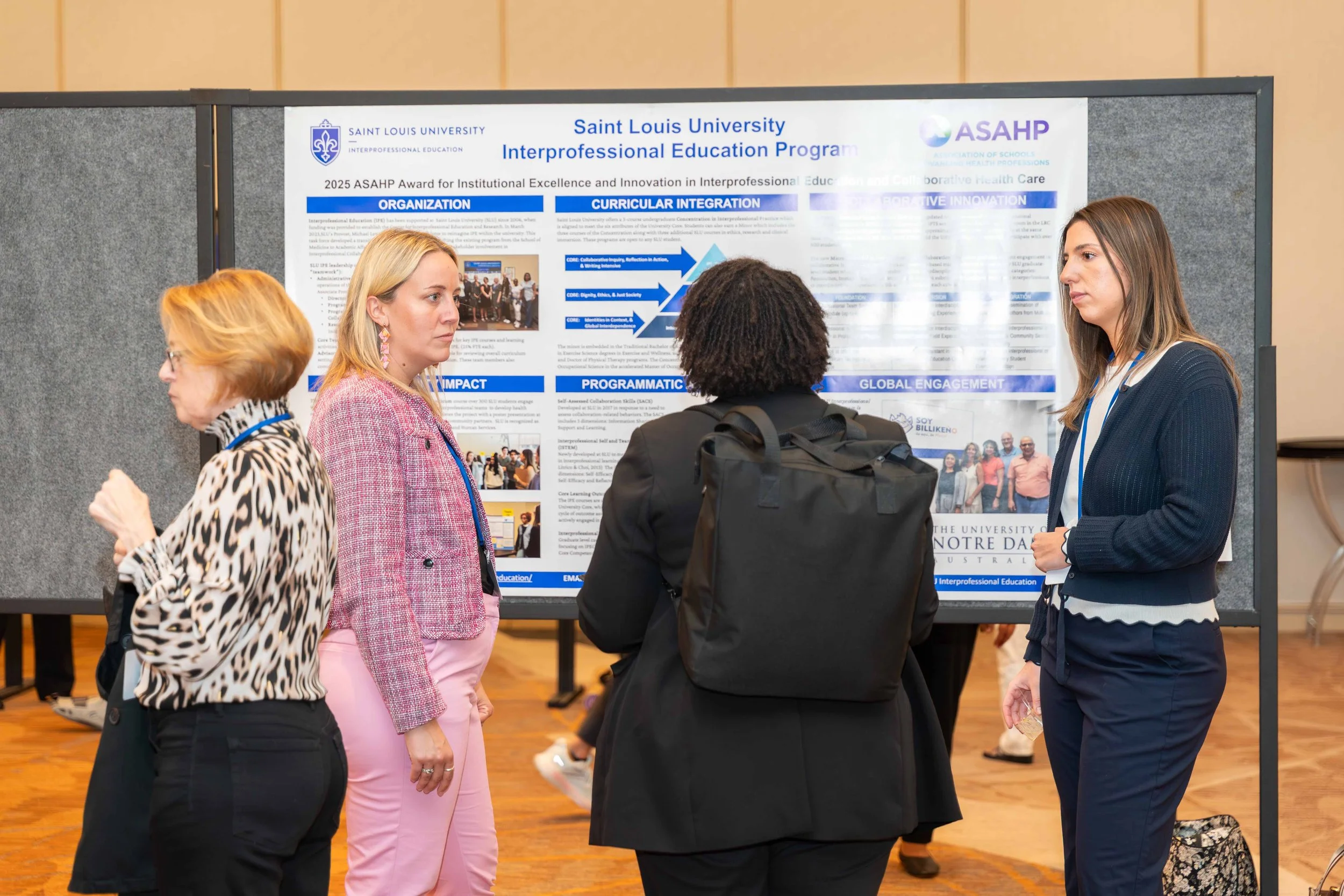 Women standing in front of a research poster at an academic conference, discussing the poster content.