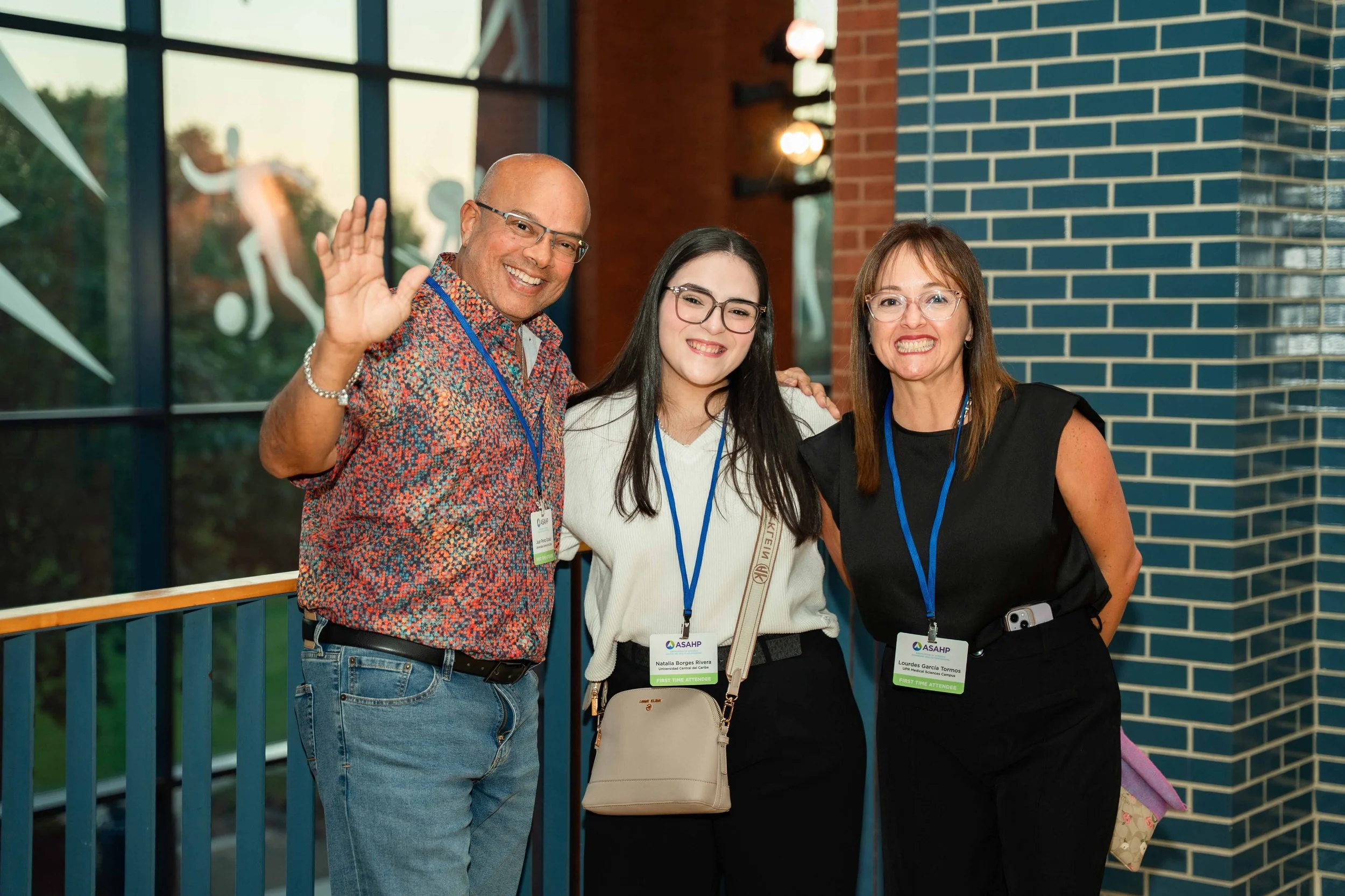 Three people standing together, smiling, at a conference, wearing name tags and lanyards.