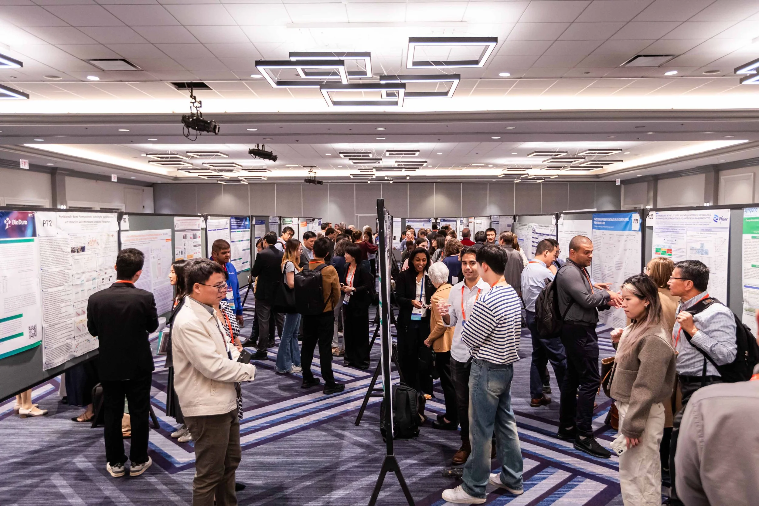 People attending a scientific conference and viewing research posters in a large, well-lit conference room.
