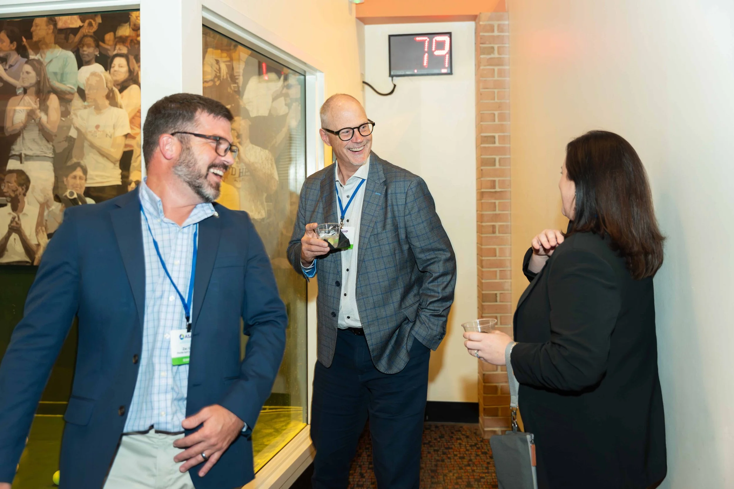 Three business professionals, two men and one woman, are engaged in a conversation at a networking event, standing near a glass tank and a digital temperature display.