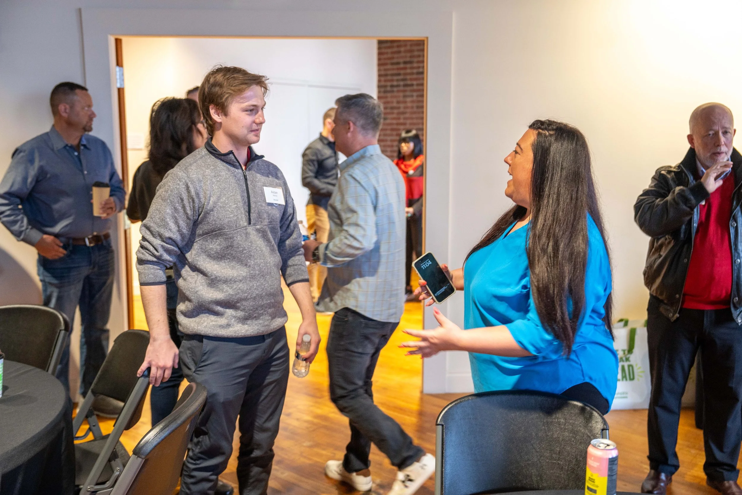 People chatting at a social gathering or networking event in a room with wood flooring and white walls.