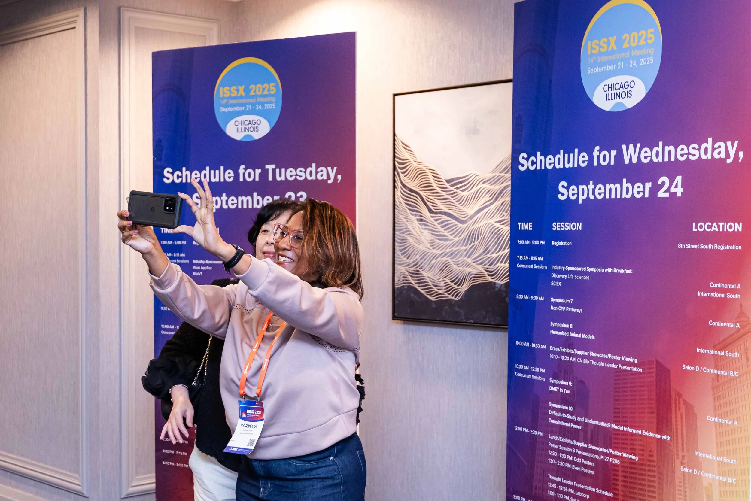 Two women taking a selfie at a conference, standing in front of a schedule poster for ISSX 2025 in Chicago, Illinois.