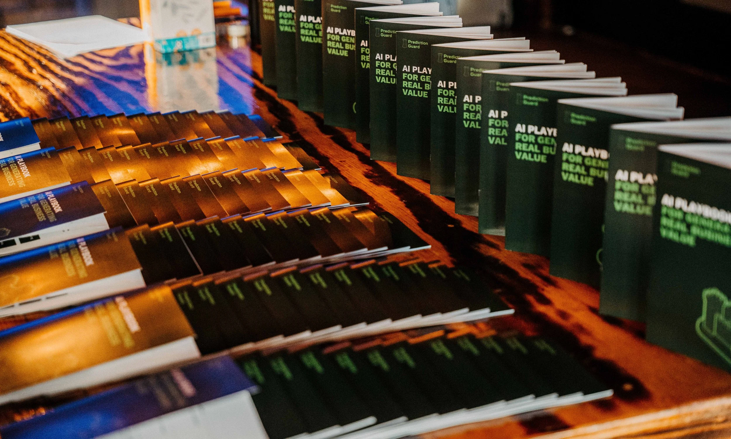Stacks of brochures and booklets, some with green and black covers and others with orange and black covers, arranged on a wooden table.