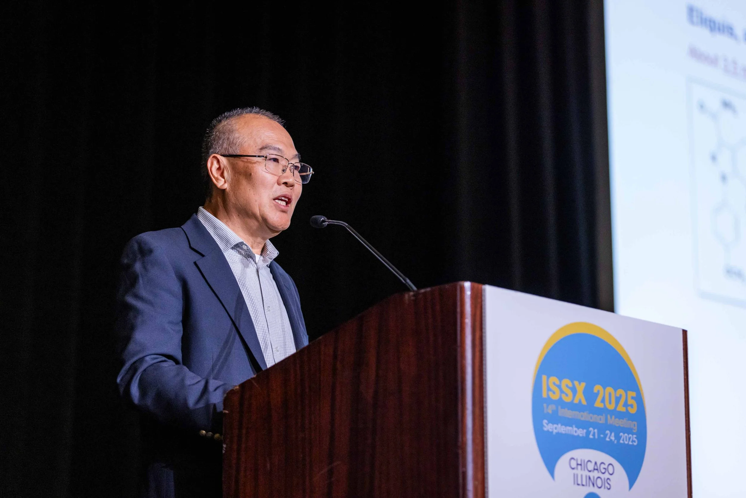 A man in a suit and glasses giving a speech at a podium during the ISSX 2025 conference in Chicago, Illinois, from September 21 to 24, 2025.