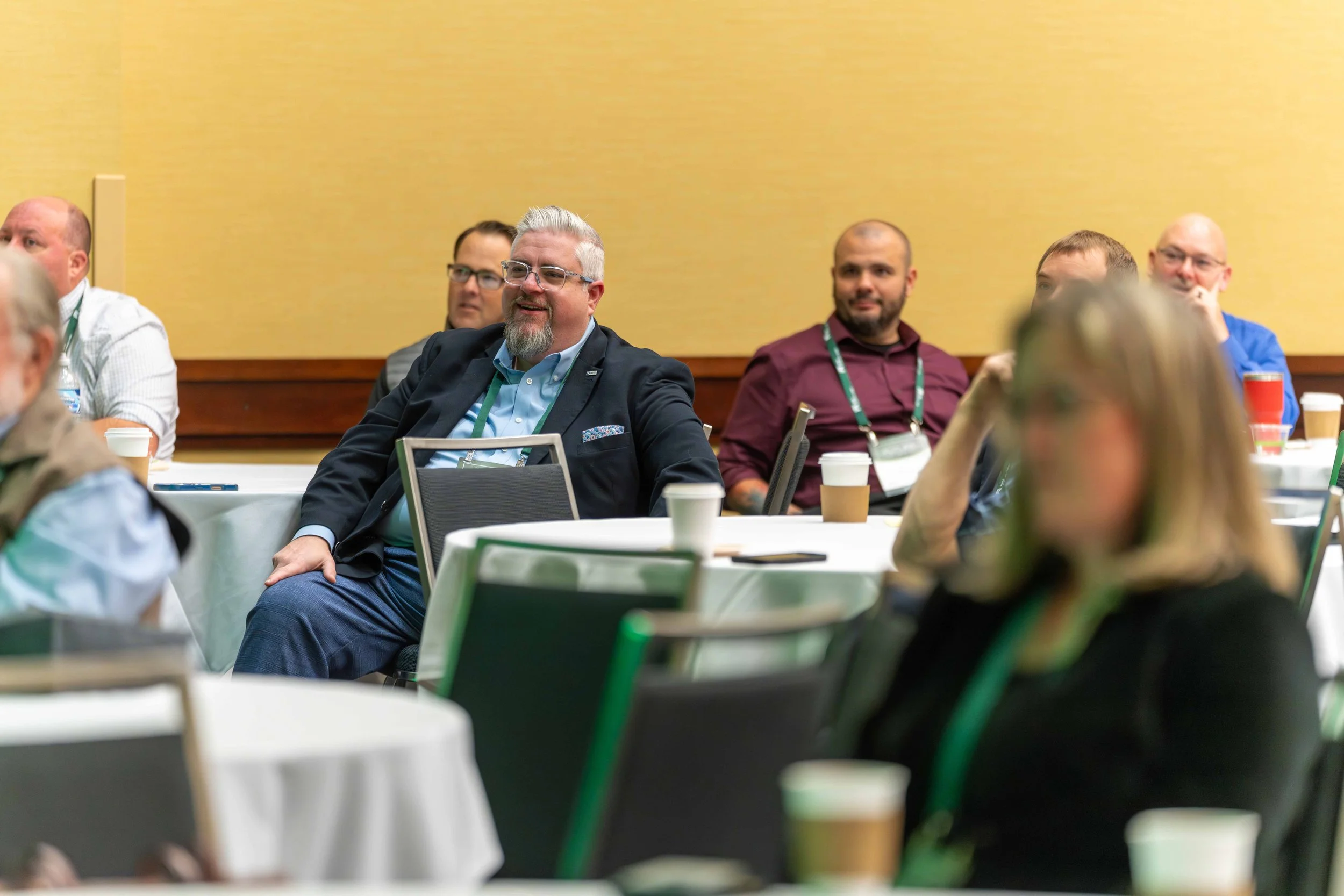 Attendees at a conference sitting at round tables, listening and smiling.
