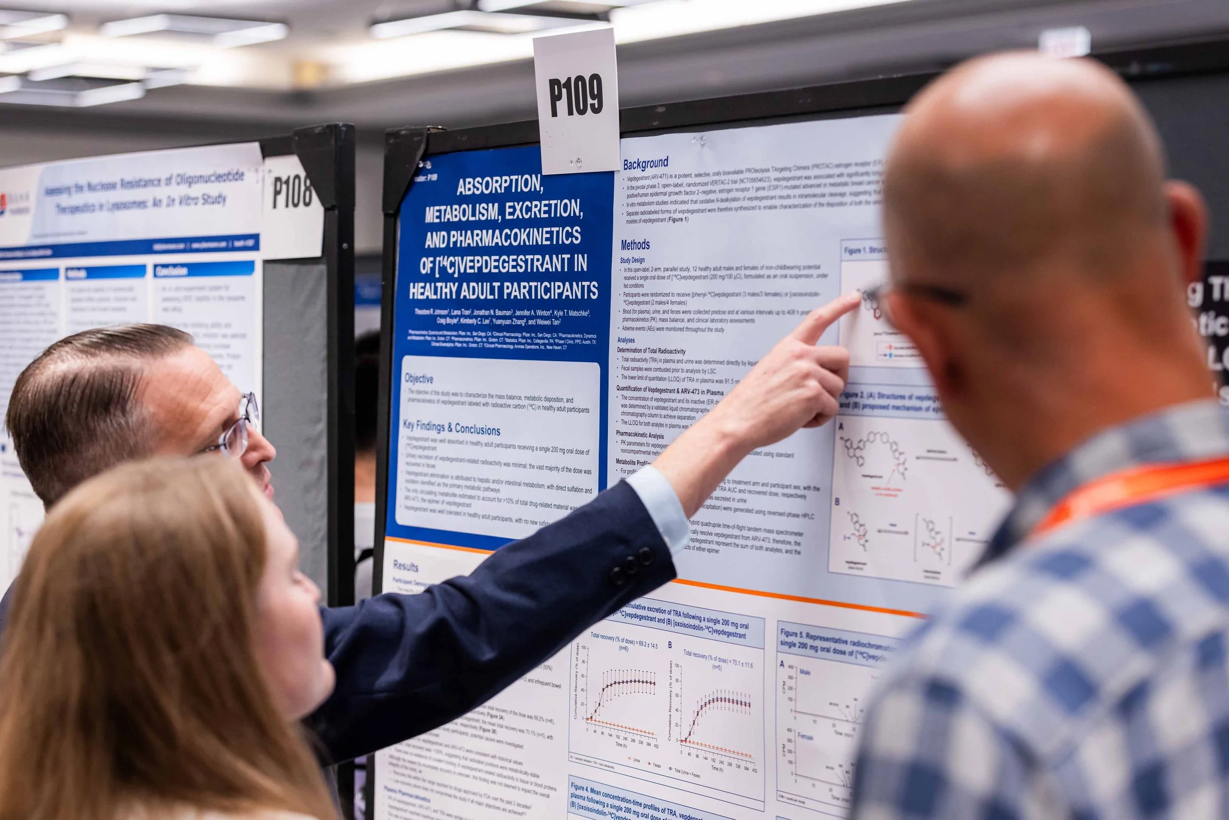 Three people discussing a scientific research poster about metabolism and excretion of a drug in adult participants at a conference.