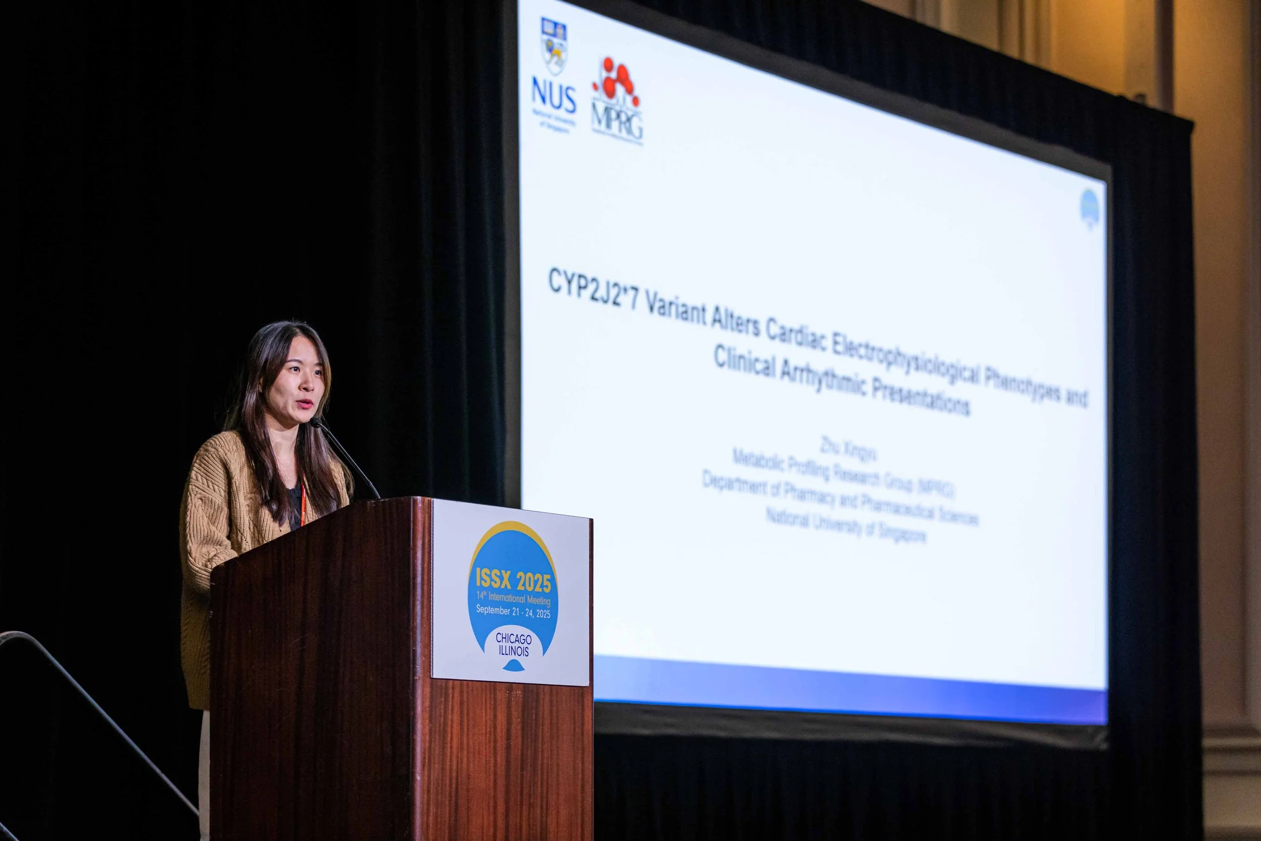 Woman giving a presentation at a conference with a large screen displaying a scientific research title. The podium has a logo for ISSX 2025 held in Chicago, Illinois.