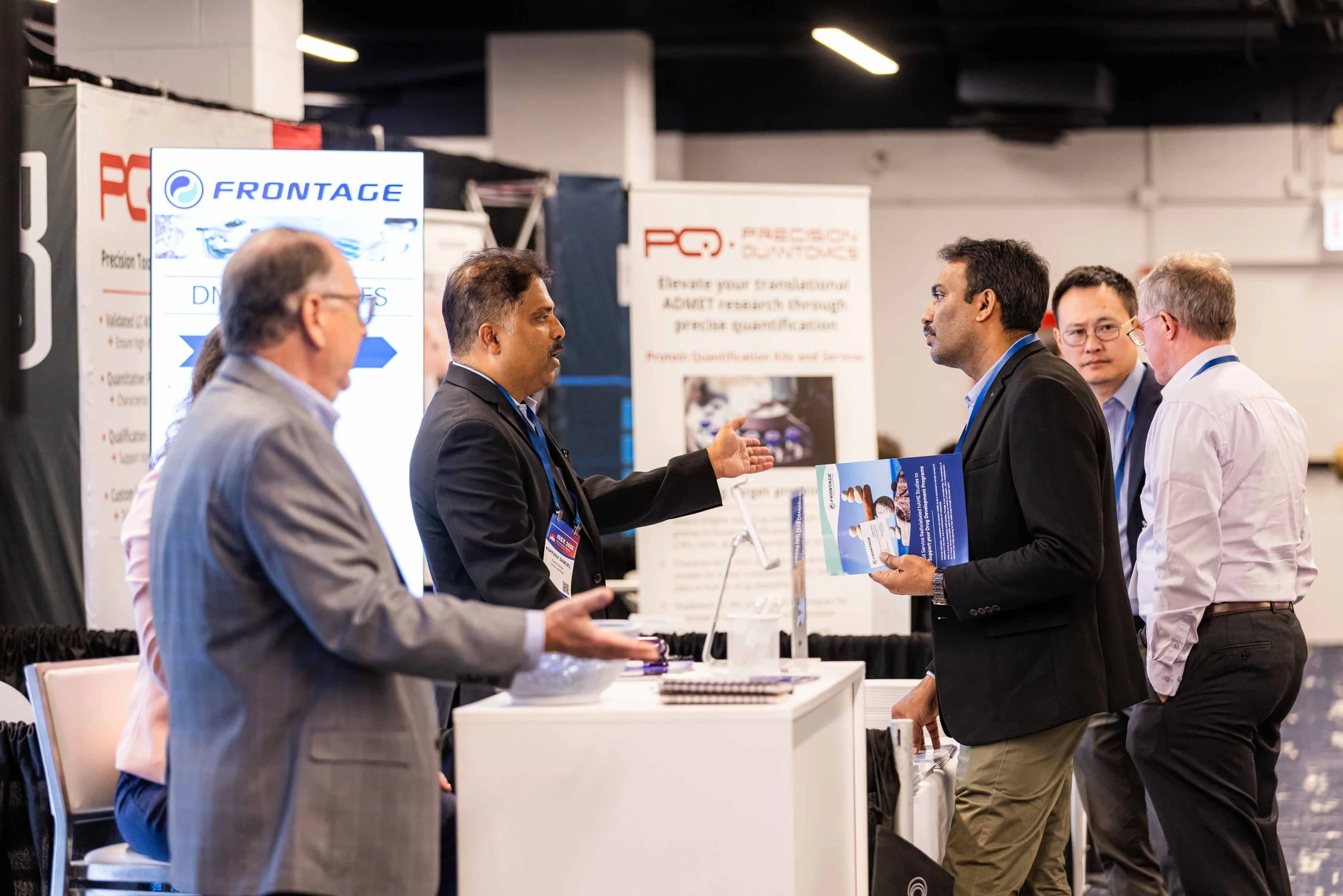 Business professionals at a conference booth engaging in discussion, with informational banners in the background.