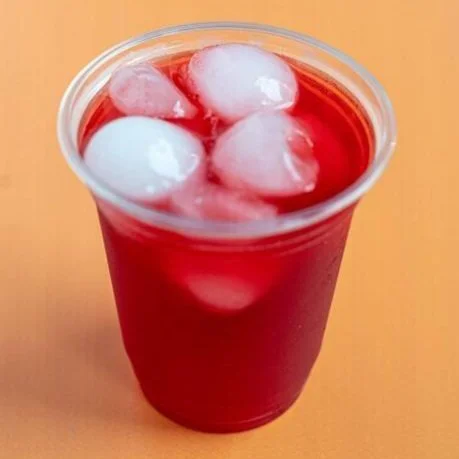 Plastic cup filled with red liquid and ice cubes on an orange background.