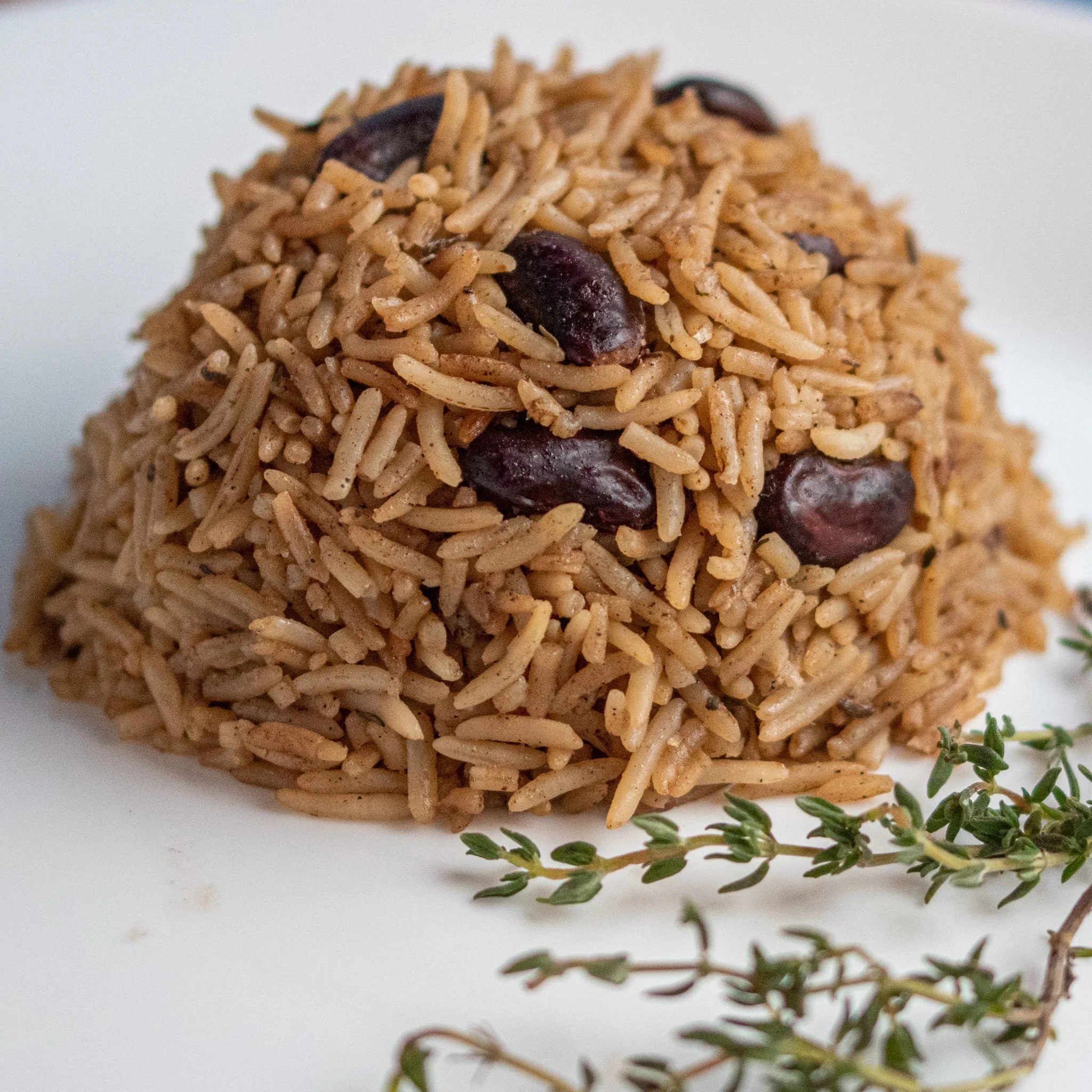 A serving of rice and beans, garnished with fresh thyme on a white plate.