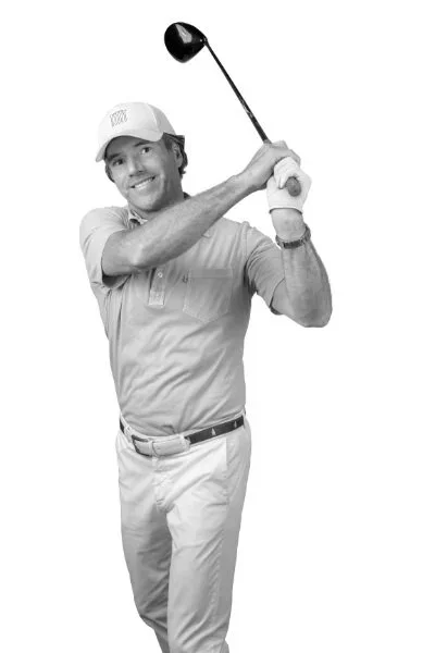 A man in a baseball cap and polo shirt holding a golf club, ready to swing.