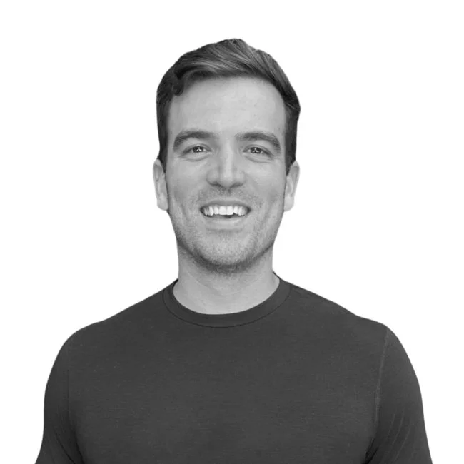 Black-and-white photo of a smiling young man with short hair wearing a dark t-shirt.