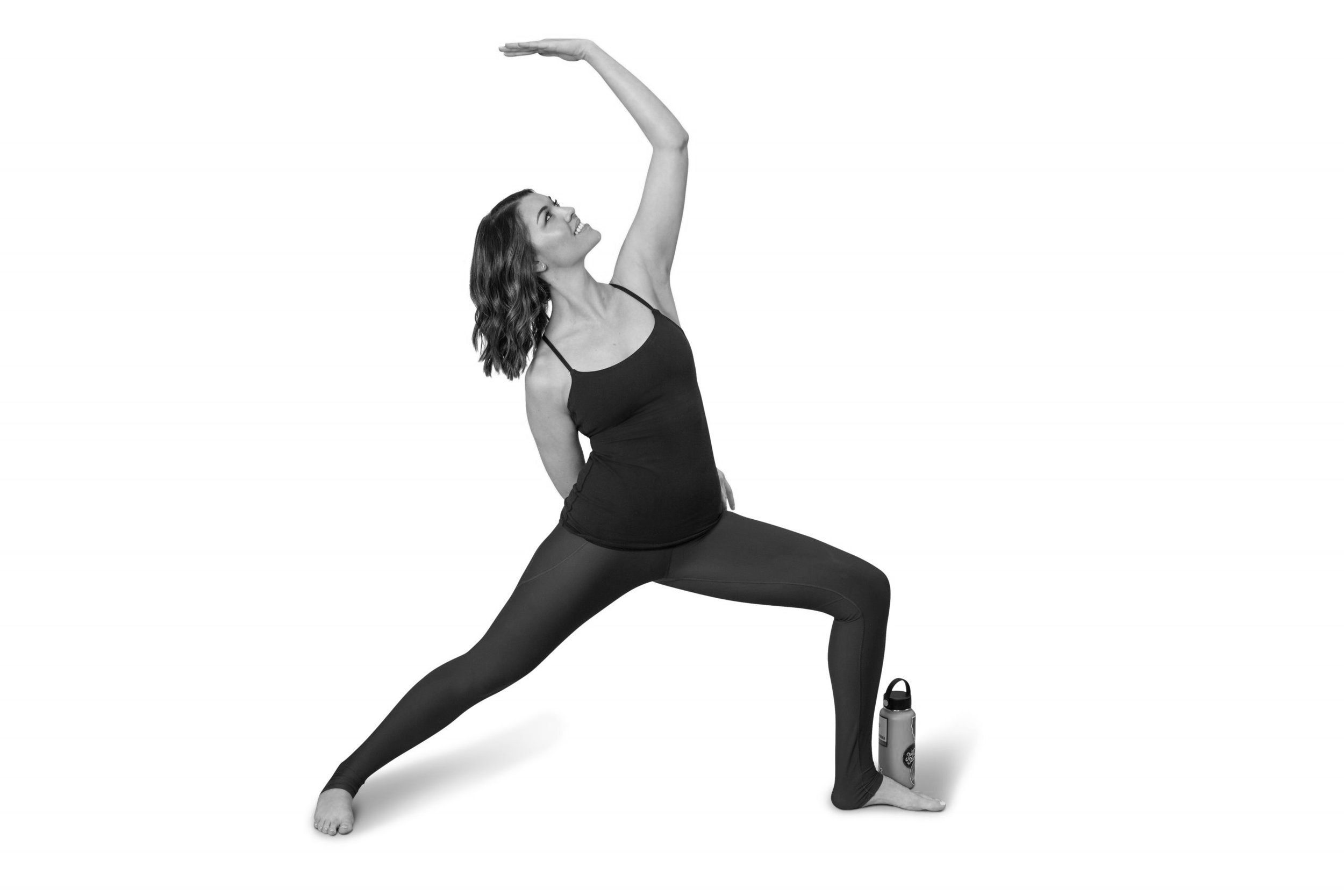 A woman practicing yoga, with one leg forward and bent at the knee, the other leg straight back, and one arm raised overhead, in a lunge pose, next to a water bottle.