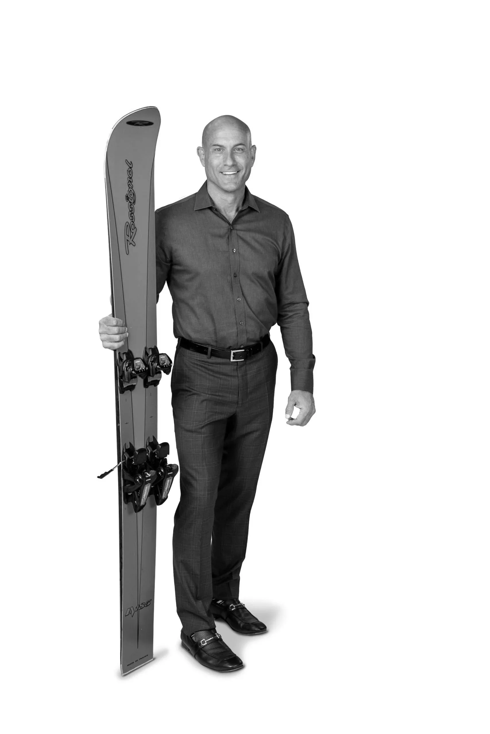 A man in dress shirt and dress pants holding a pair of skis.