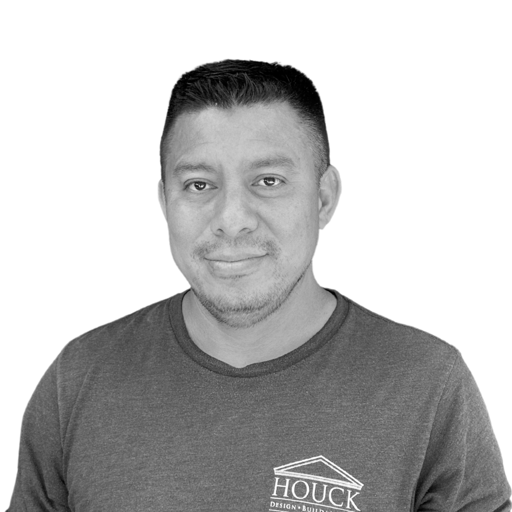 Black and white portrait of a man with short dark hair, slight beard, wearing a dark T-shirt with a logo on the chest, against a plain background.