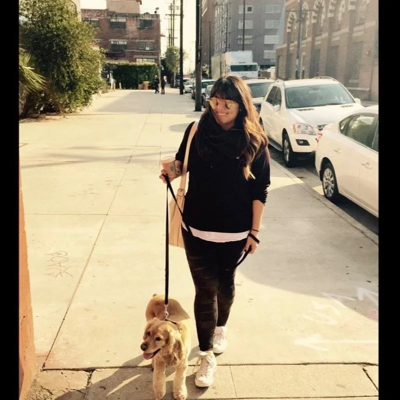 Woman walking a golden retriever puppy on a city sidewalk during daytime.